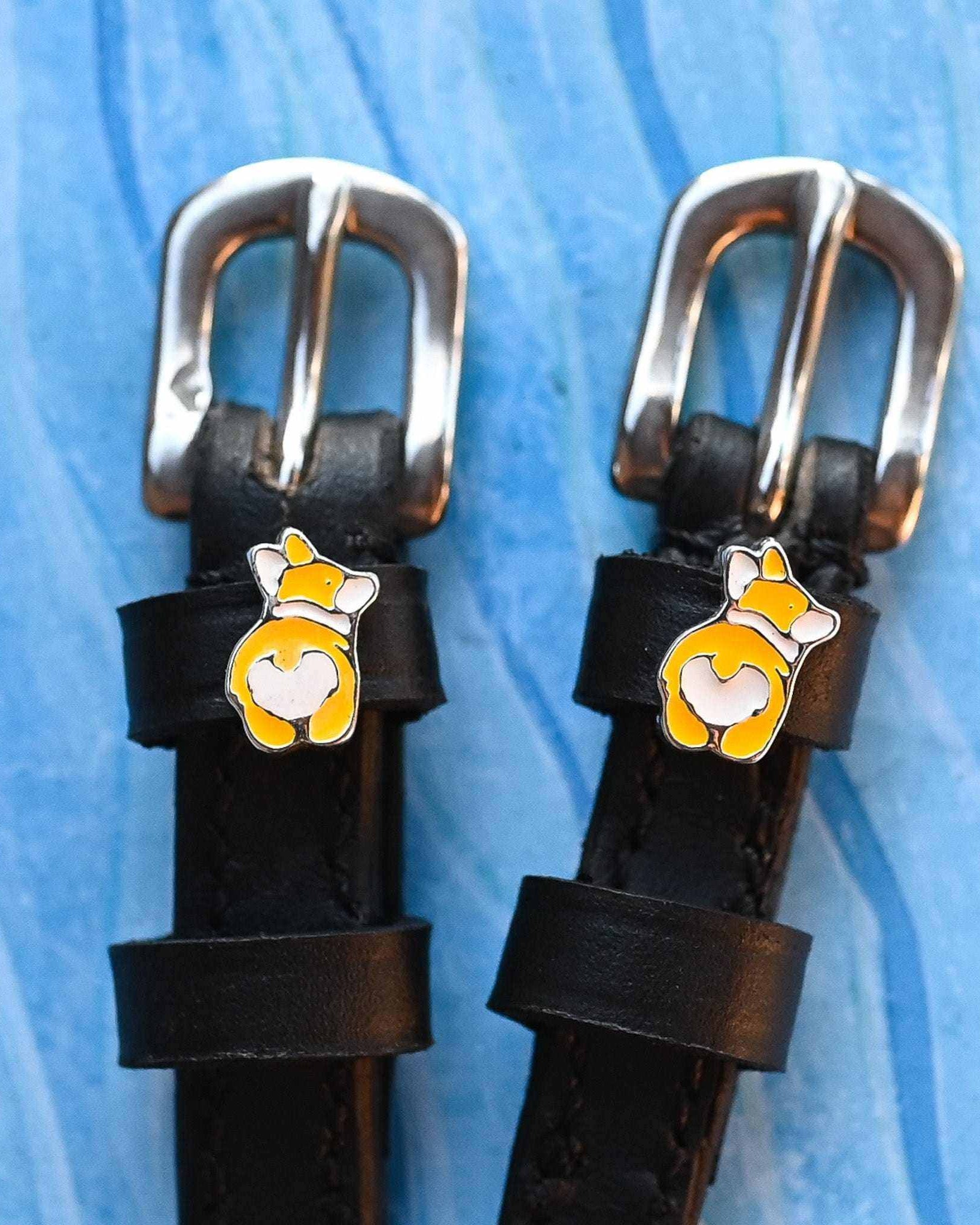 Two corgi butt charms on black leather spur straps over blue texture