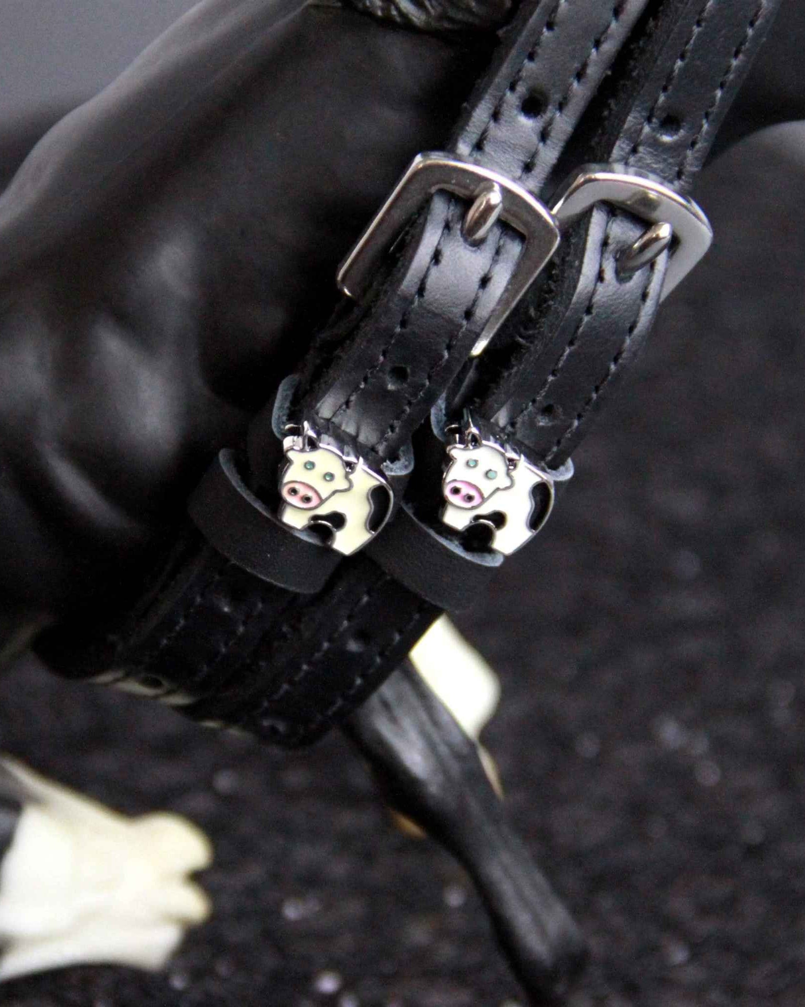 Black leather cow spur straps fastened on a model horse's leg, ManeJane enamel cow charm detail