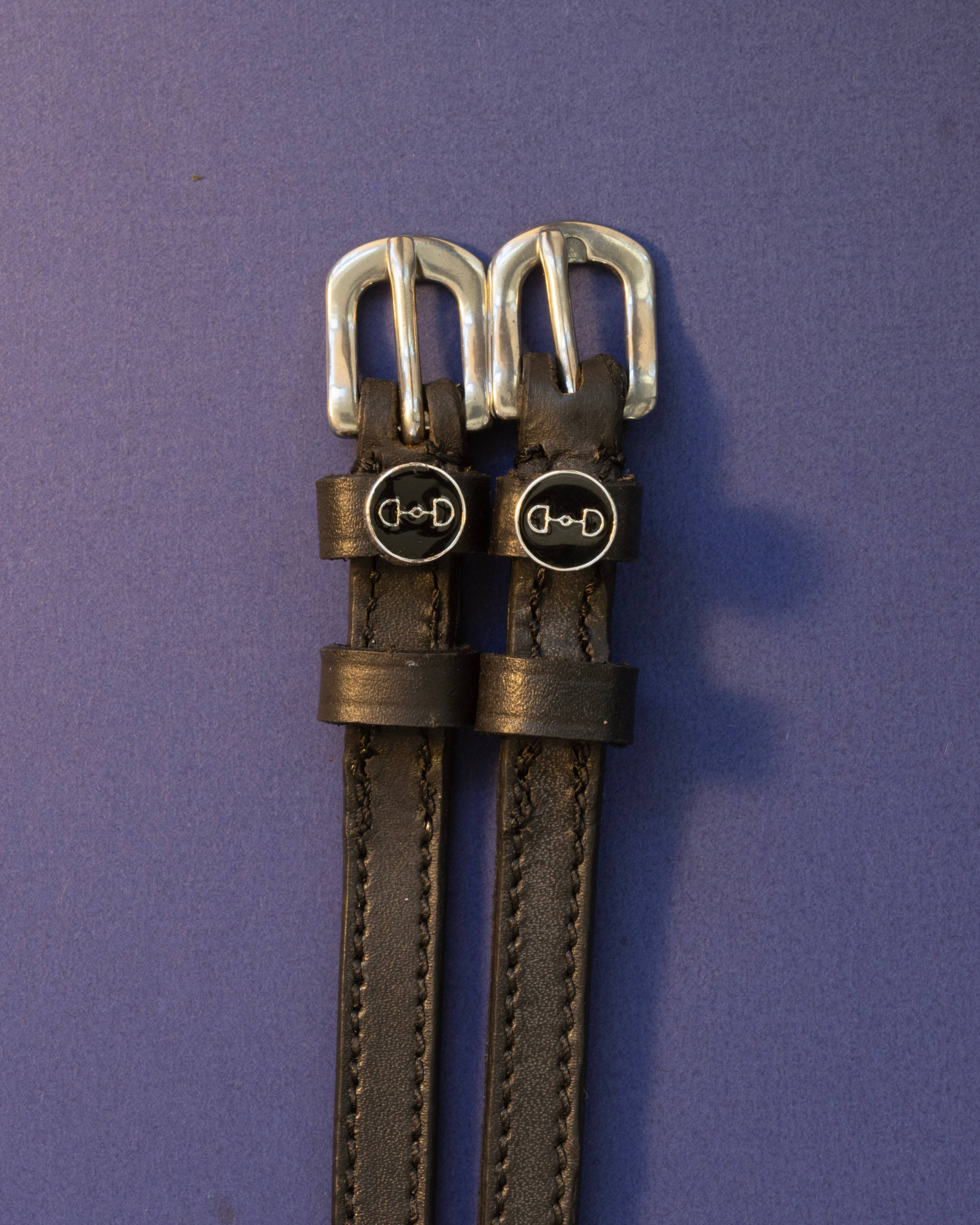 Black leather bit-charm spur straps laid flat on a purple background