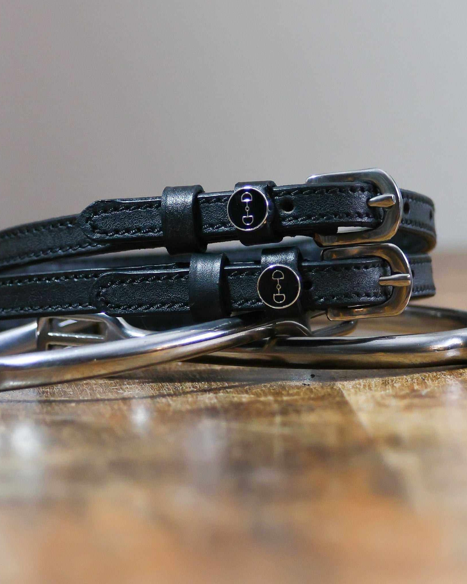 Black leather D-ring spur straps coiled on wood beside a stirrup