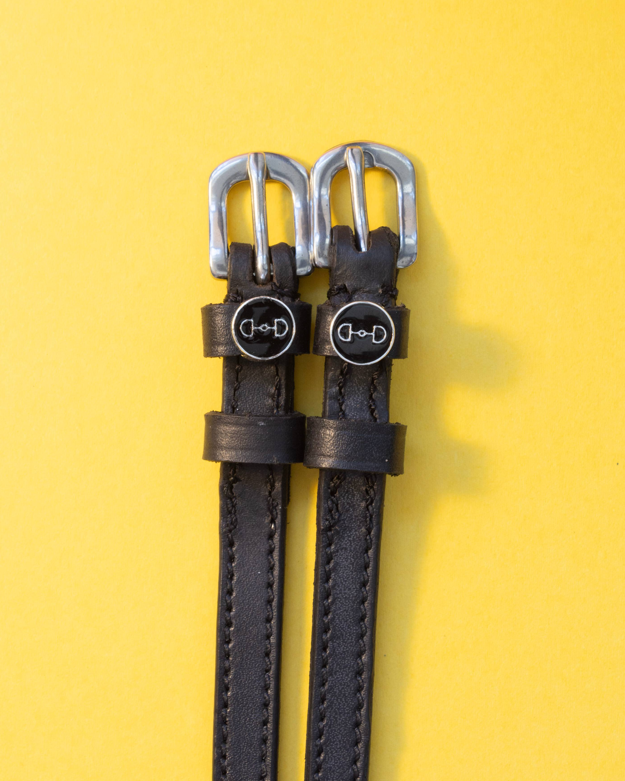 Pair of snaffle-bit charm spur straps laid flat on a yellow background