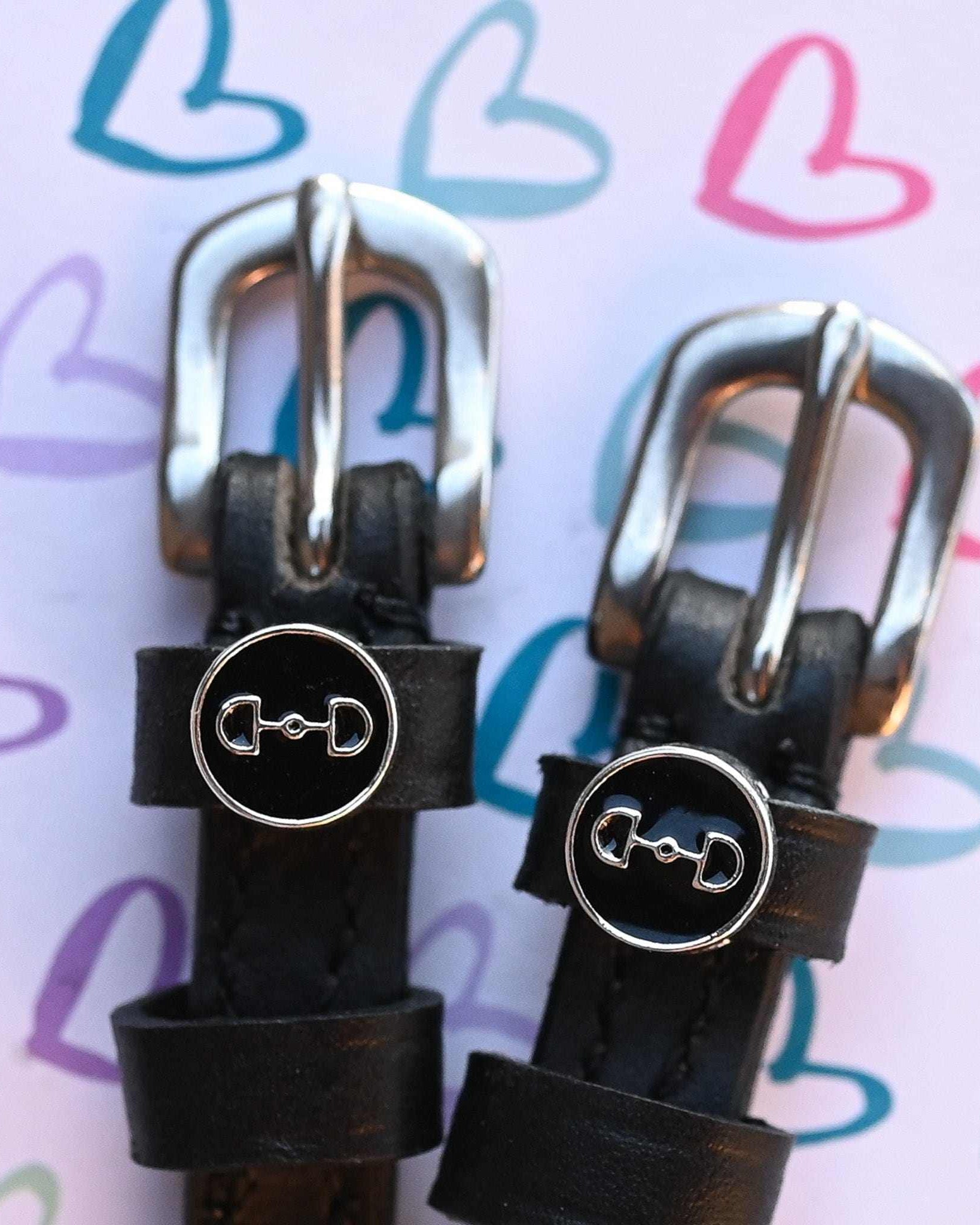 D-ring bit charm spur straps on a pastel heart-doodle backdrop, buckle close-up