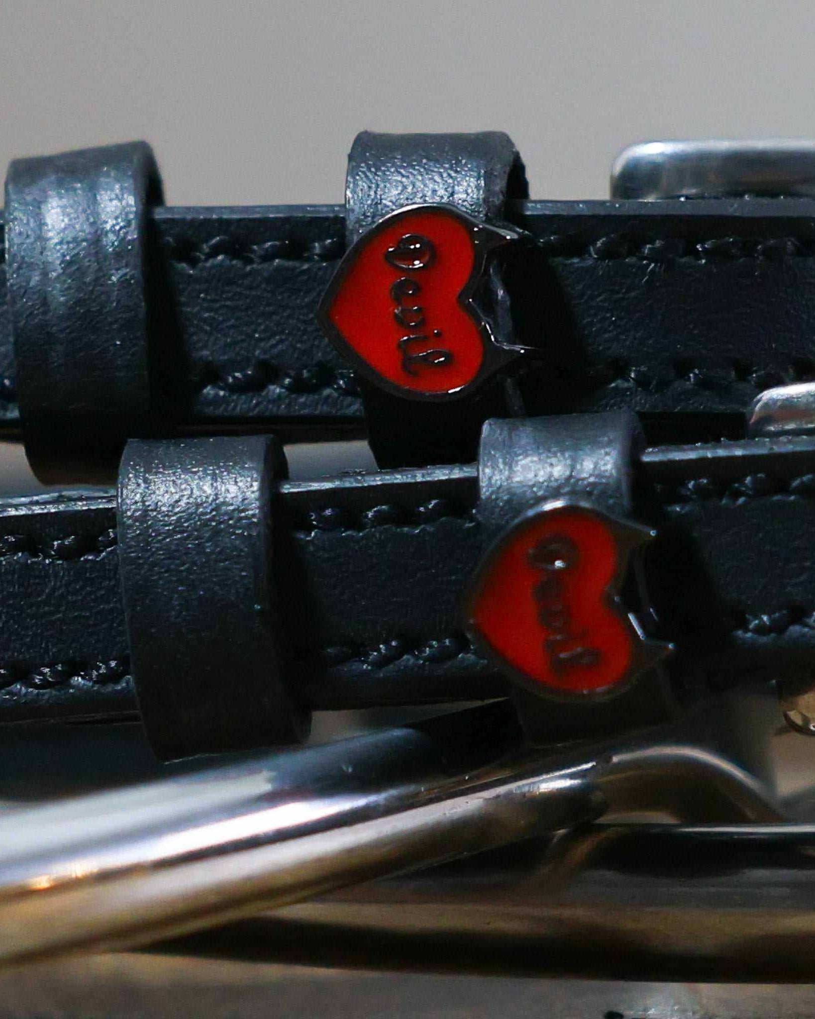 Close-up of red enamel Devil heart charms on black leather spur strap keepers