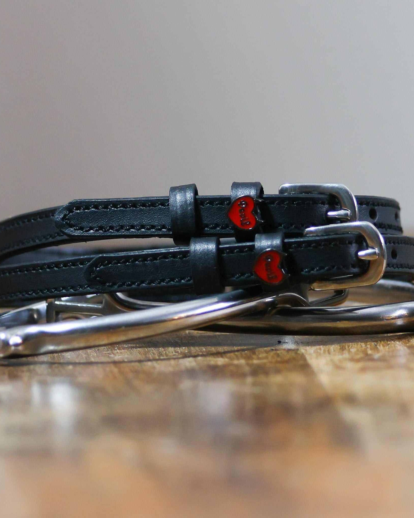 Black Devil heart spur straps coiled around a silver spur on a wooden surface