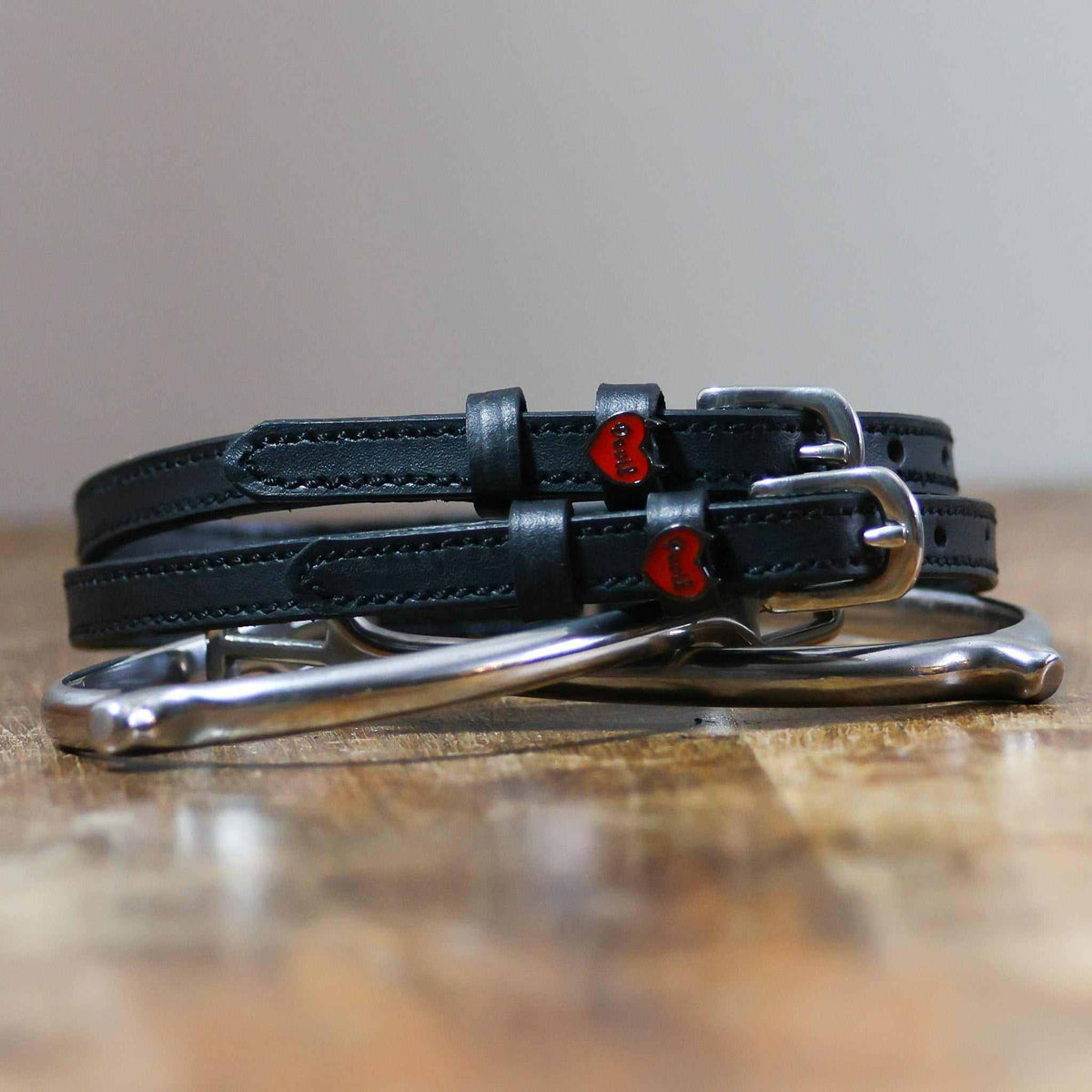 Black Devil heart spur straps coiled around a silver spur on a wooden surface