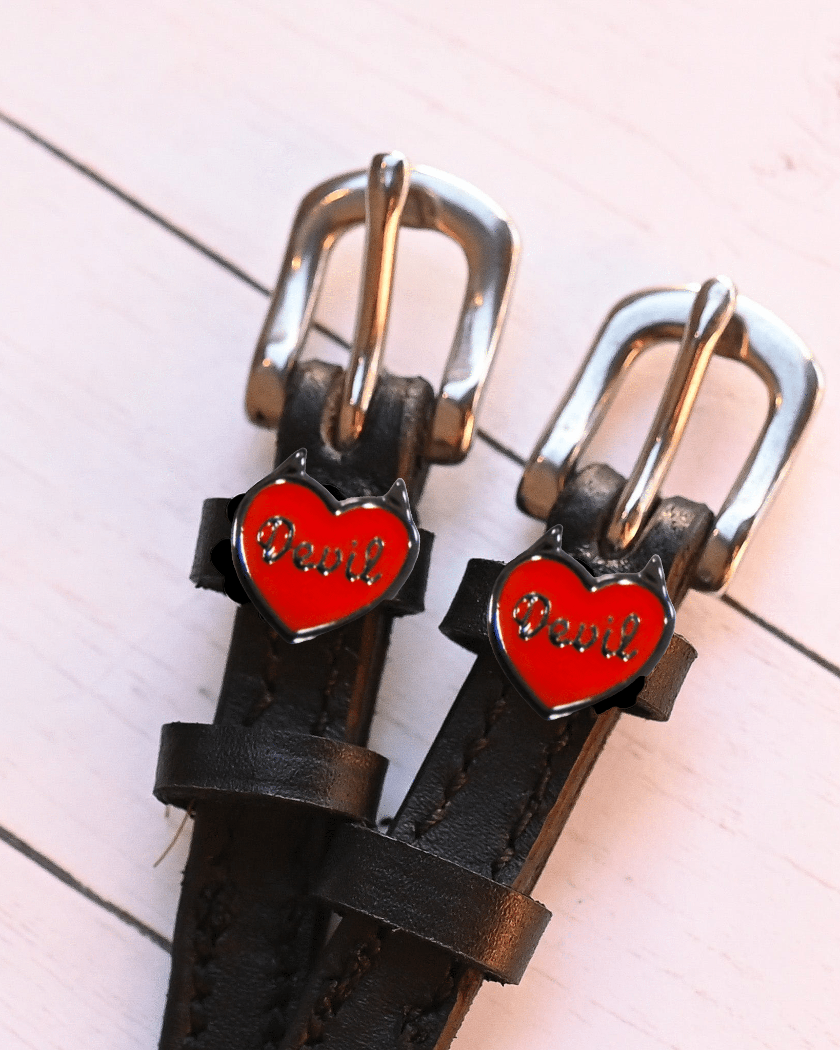 Red Devil heart charms on black spur straps against white-washed wood planks