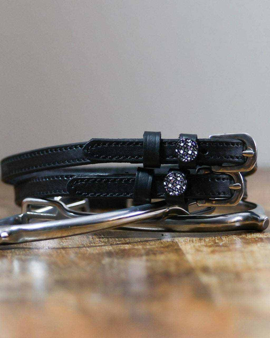 Black leather disco ball spur straps coiled beside a silver spur on a wood surface
