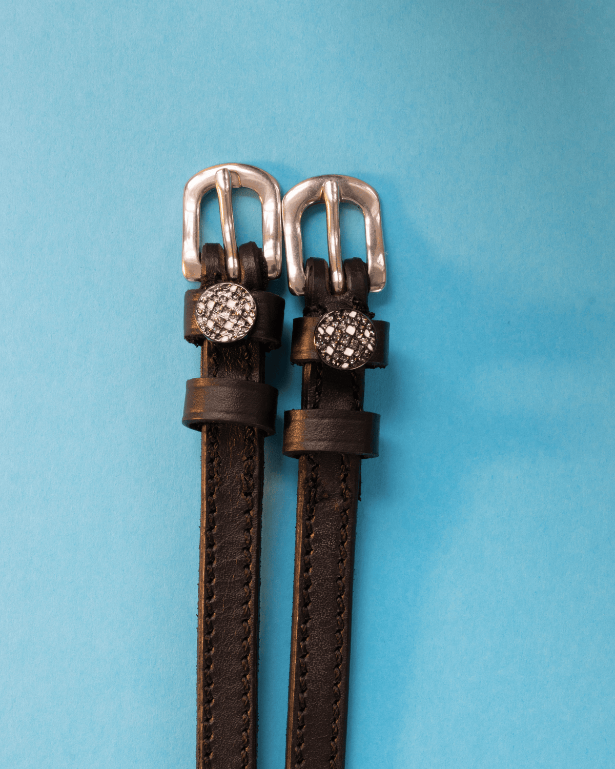 Dark brown leather disco ball spur straps with silver buckles on a light blue background