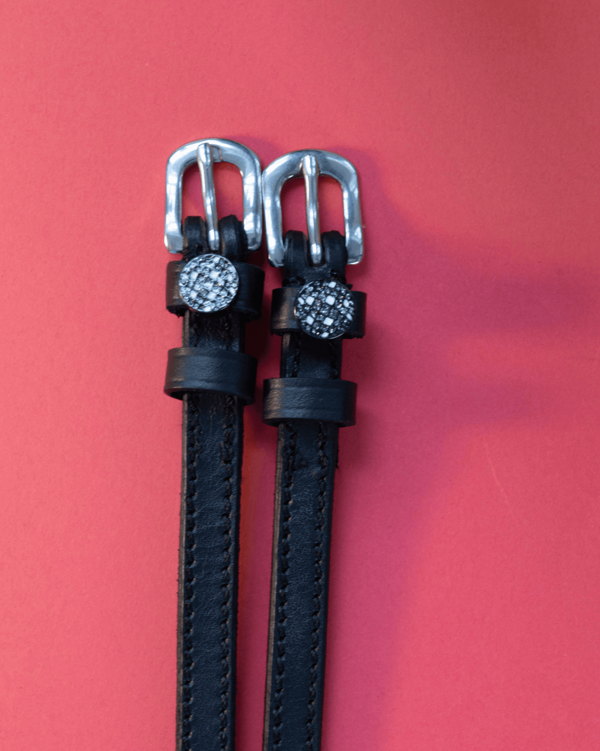 Sparkling disco ball spur straps in black leather with silver buckles on a red background