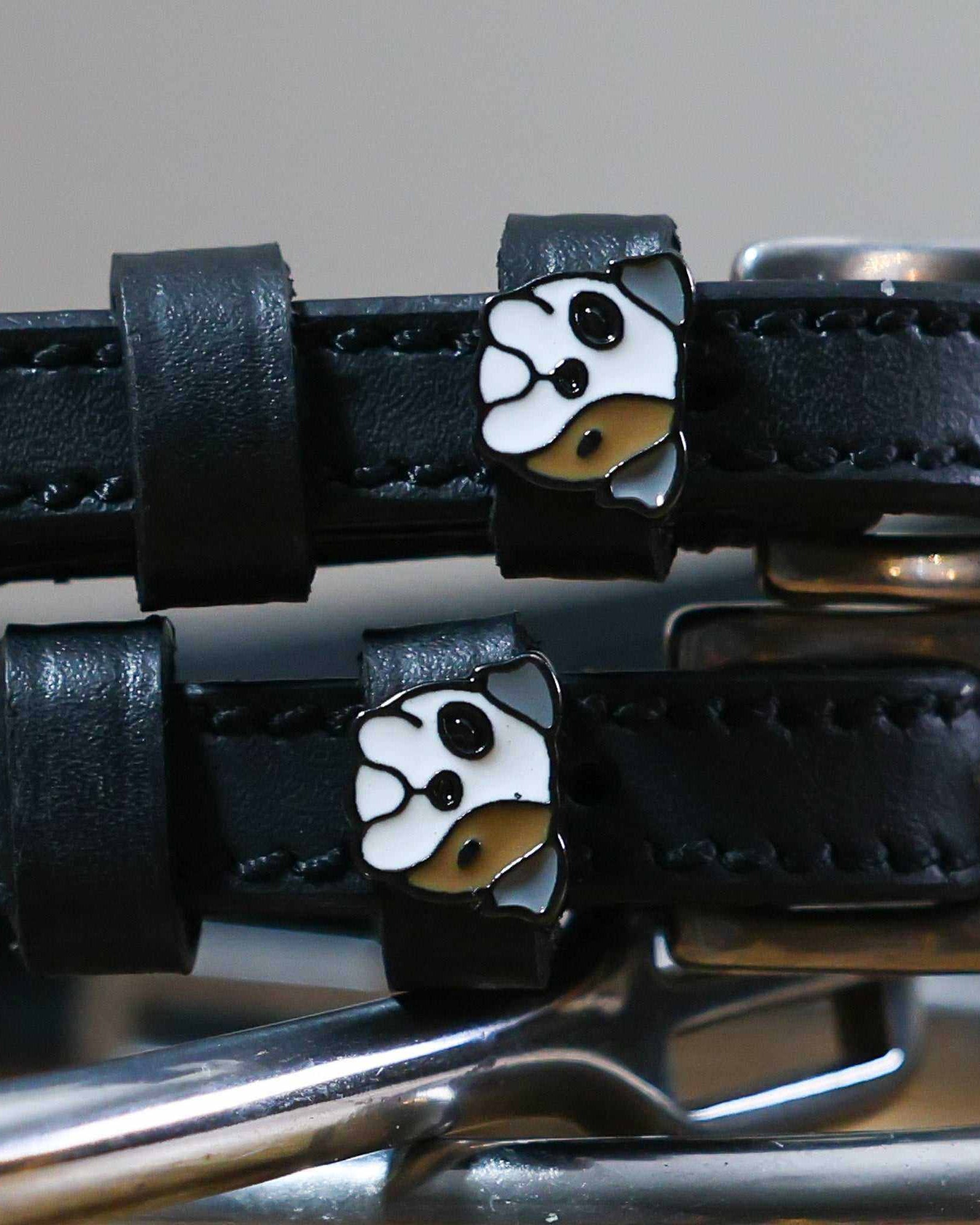 Close-up of white-and-tan bulldog head charms on black leather spur straps