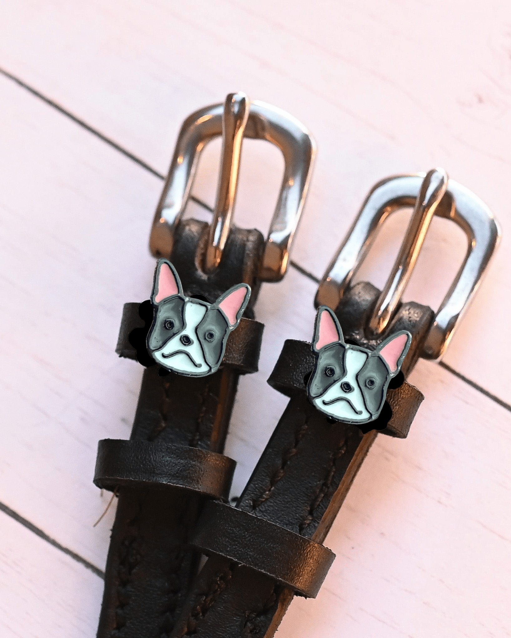 Angled close-up of French bulldog charms on ManeJane spur straps over pink planks
