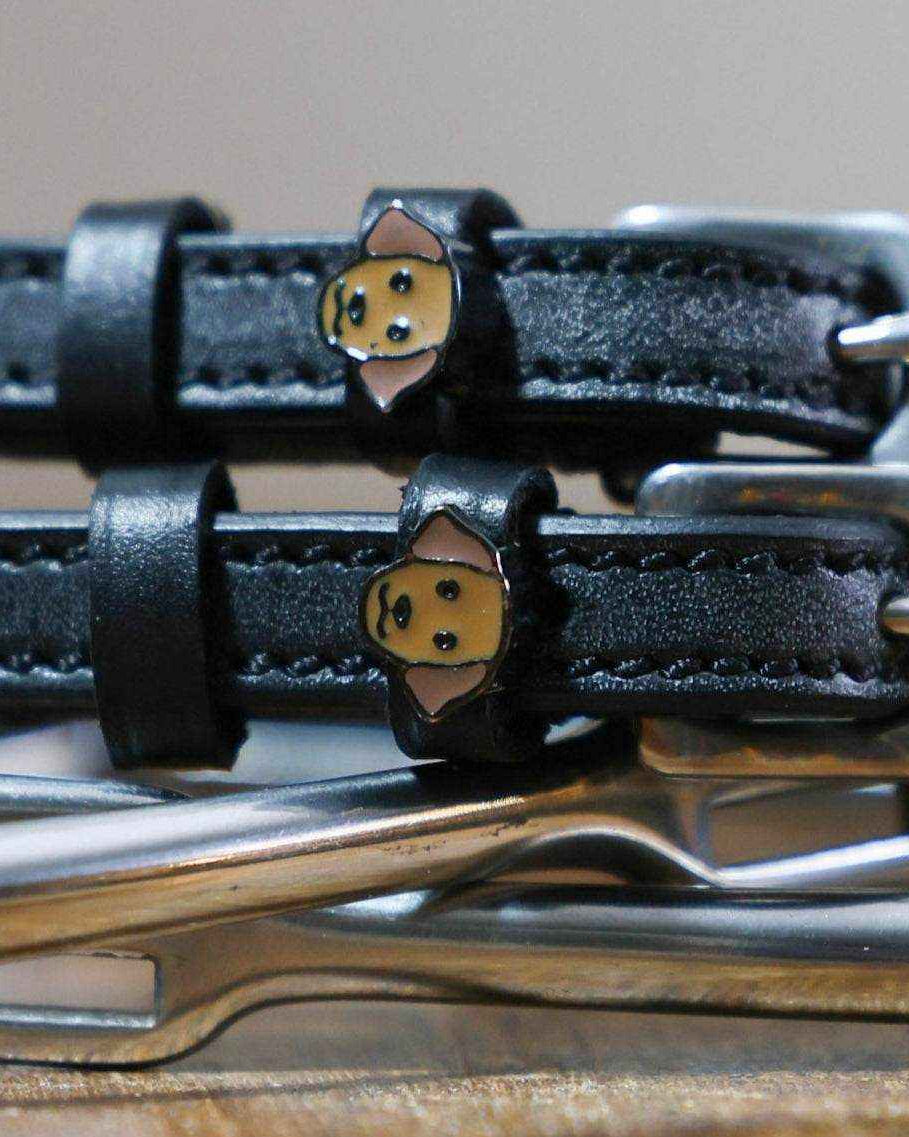 Close-up of tan Labrador dog face charms on black leather ManeJane spur straps