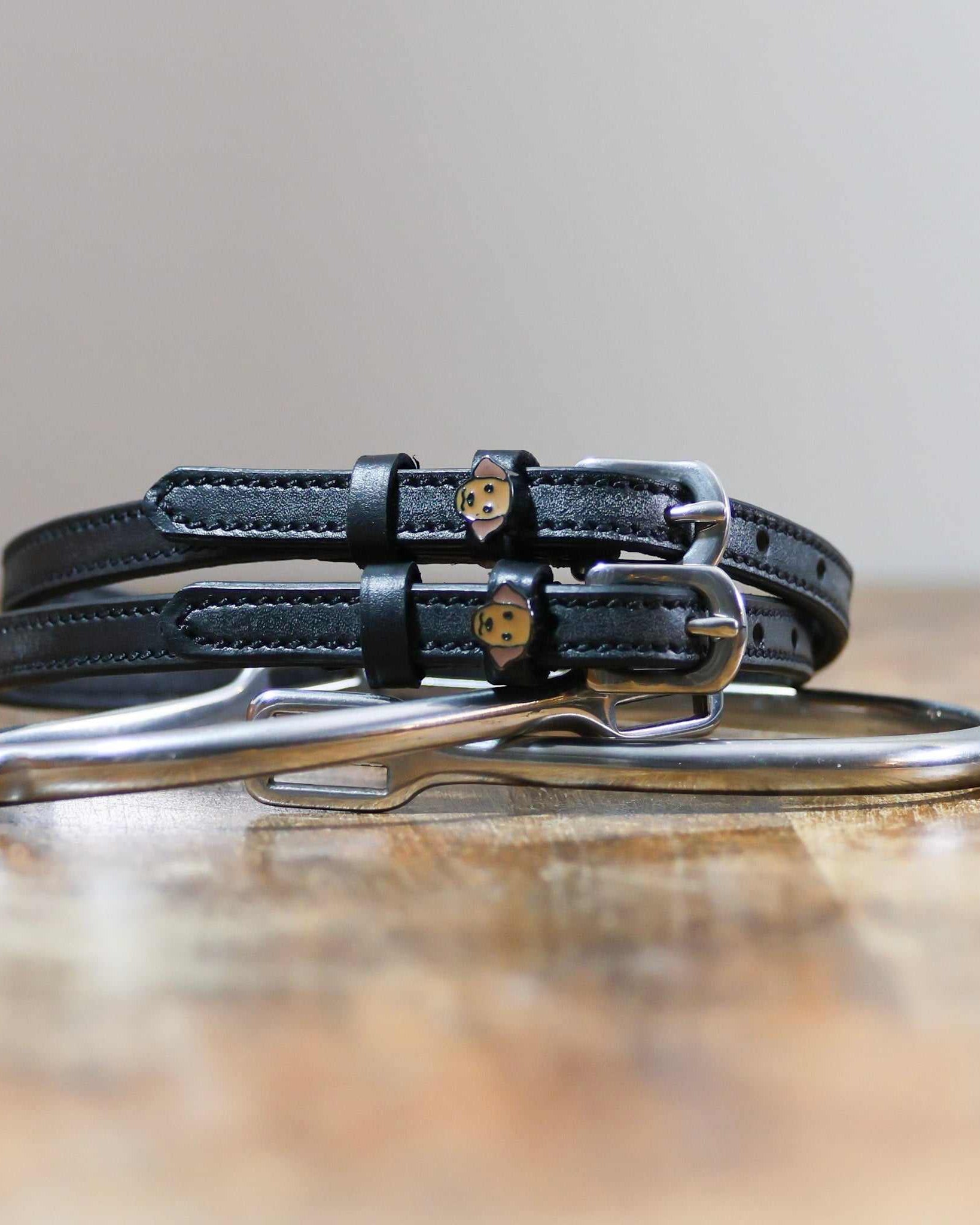 Coiled black leather Labrador spur straps resting on a silver spur, golden dog face charms