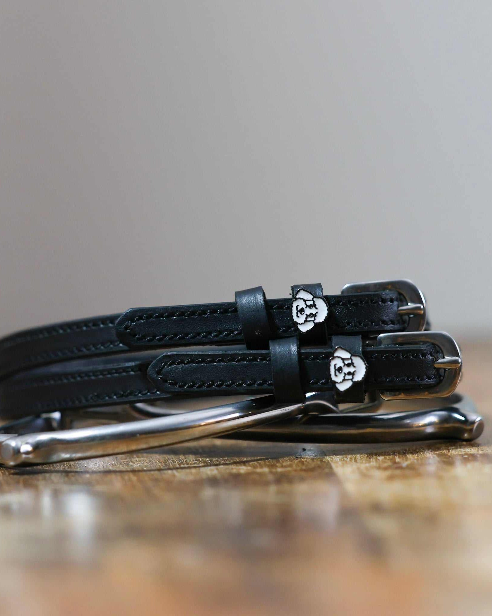 Black leather poodle spur straps stacked on a silver spur on wood, close-up