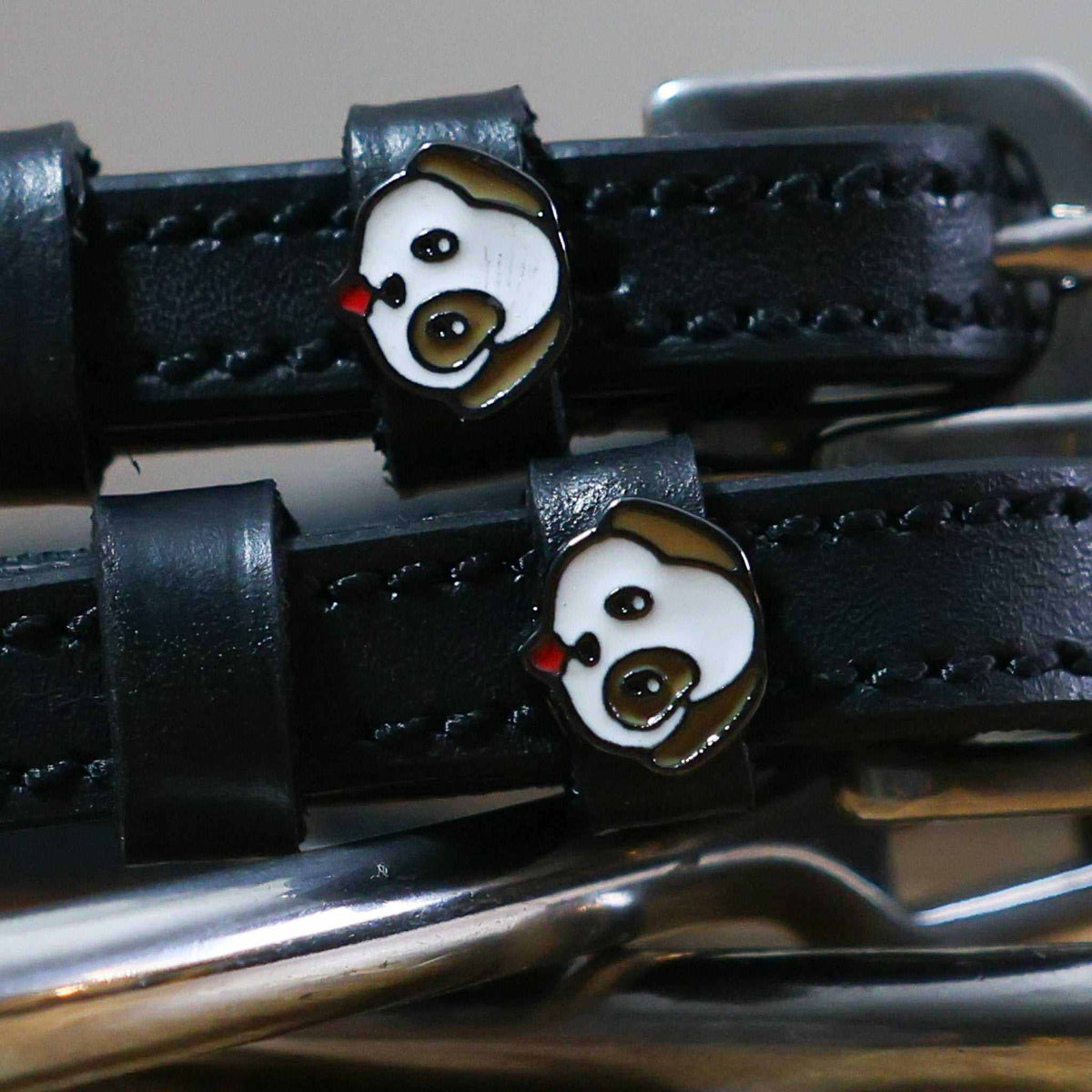 Close-up of a white-and-brown puppy face charm on a black leather spur strap