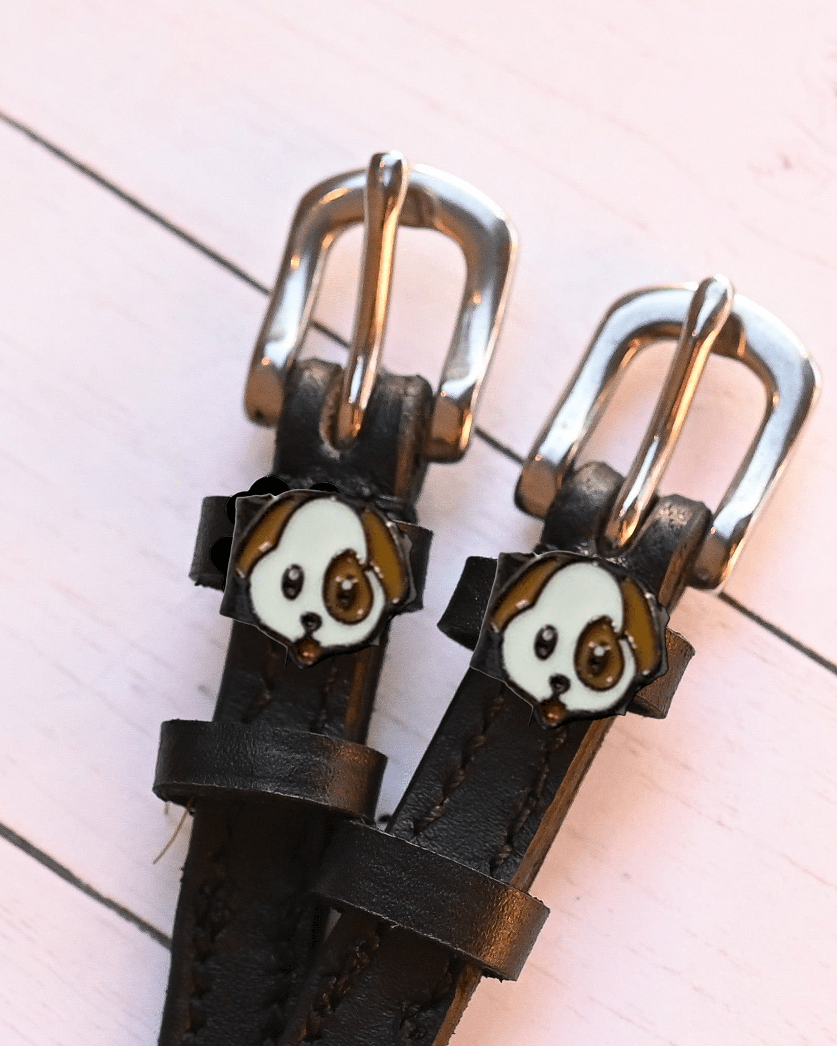 Two puppy face charms on dark brown leather spur straps over pink planks
