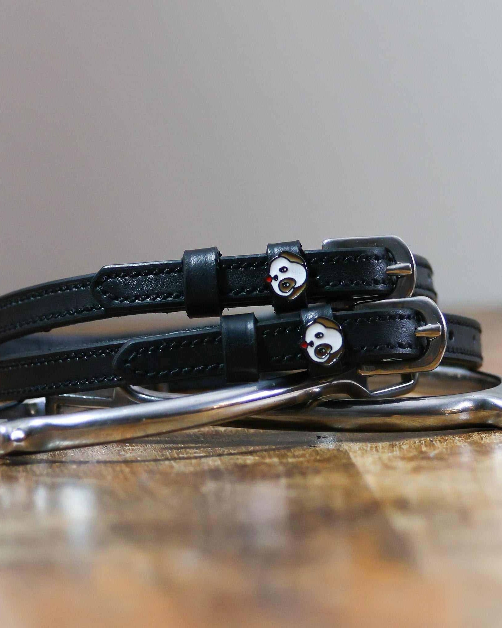 Black leather puppy face spur straps coiled beside a spur on wood