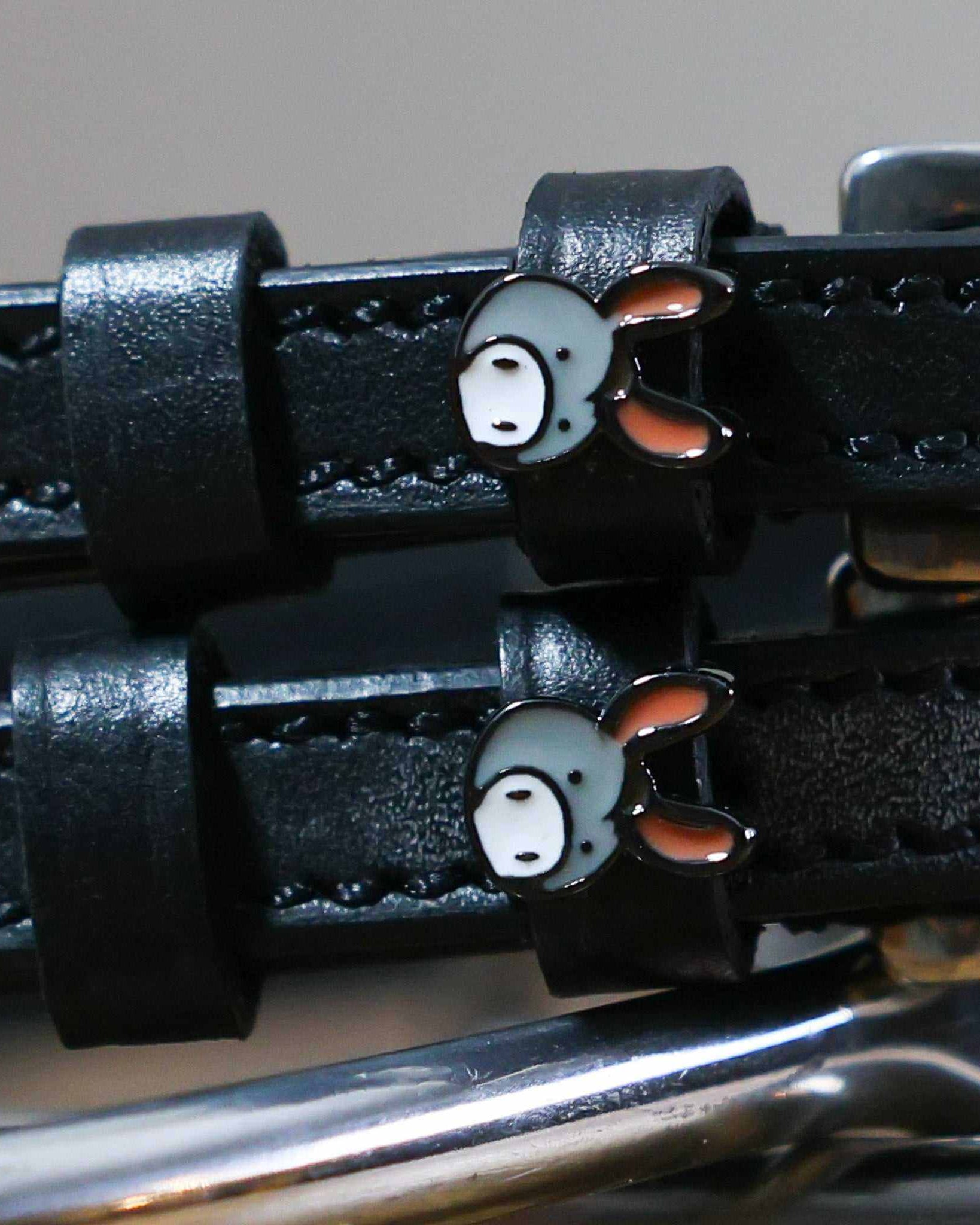 Close-up of grey donkey face charms on black leather ManeJane spur strap keepers