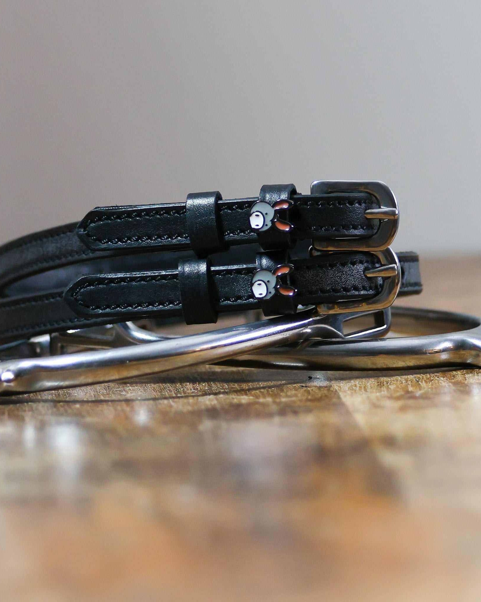 Black leather donkey spur straps coiled beside a silver stirrup on a wooden surface