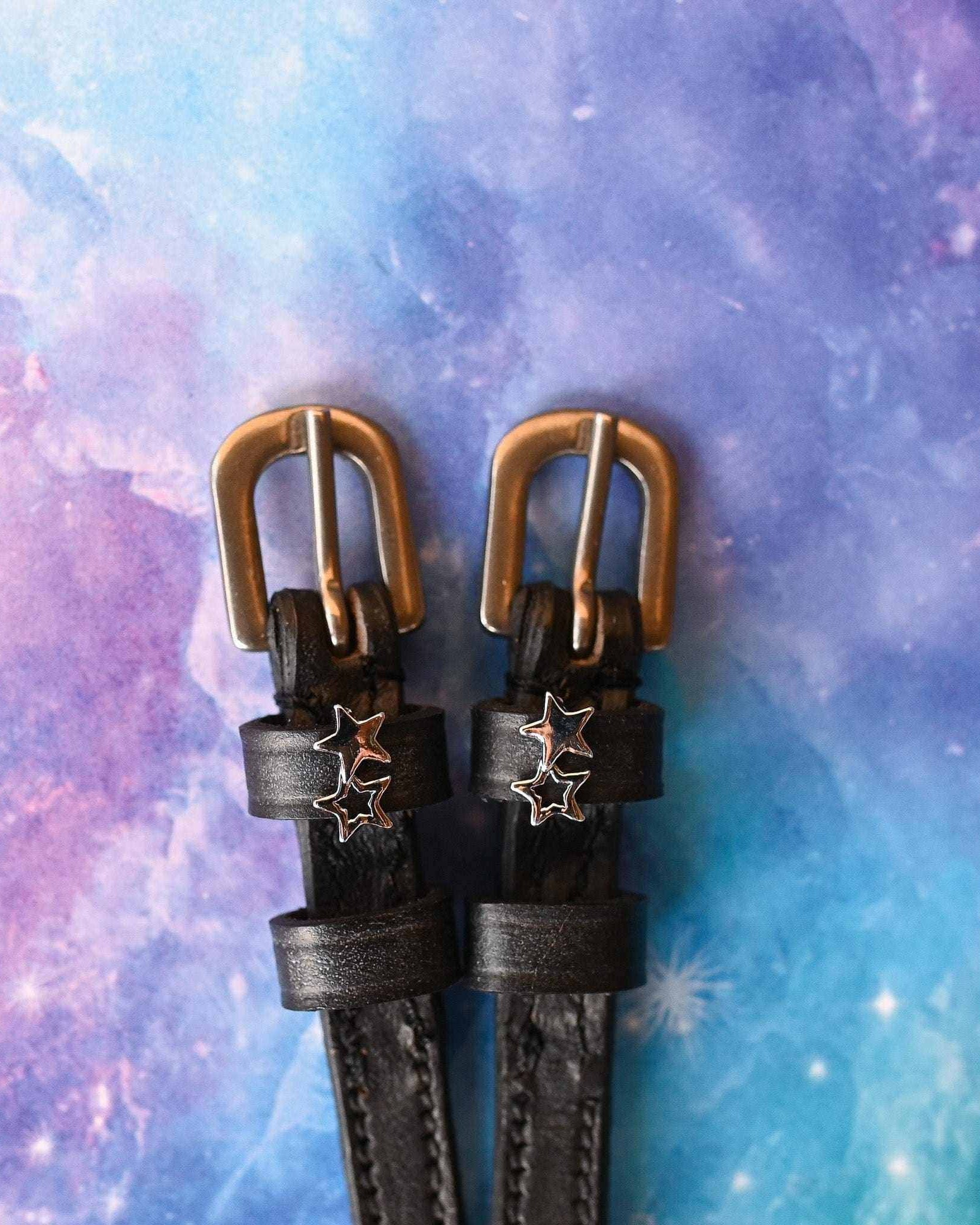 Black leather double star spur straps with brass buckles on a galaxy backdrop