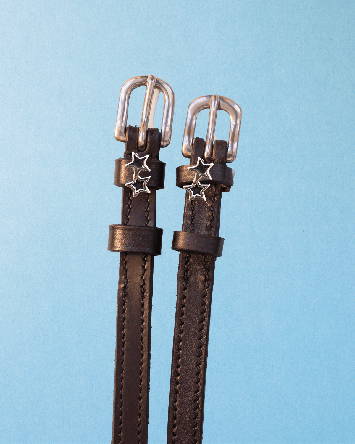 Dark brown leather double star spur straps with silver buckles on light blue