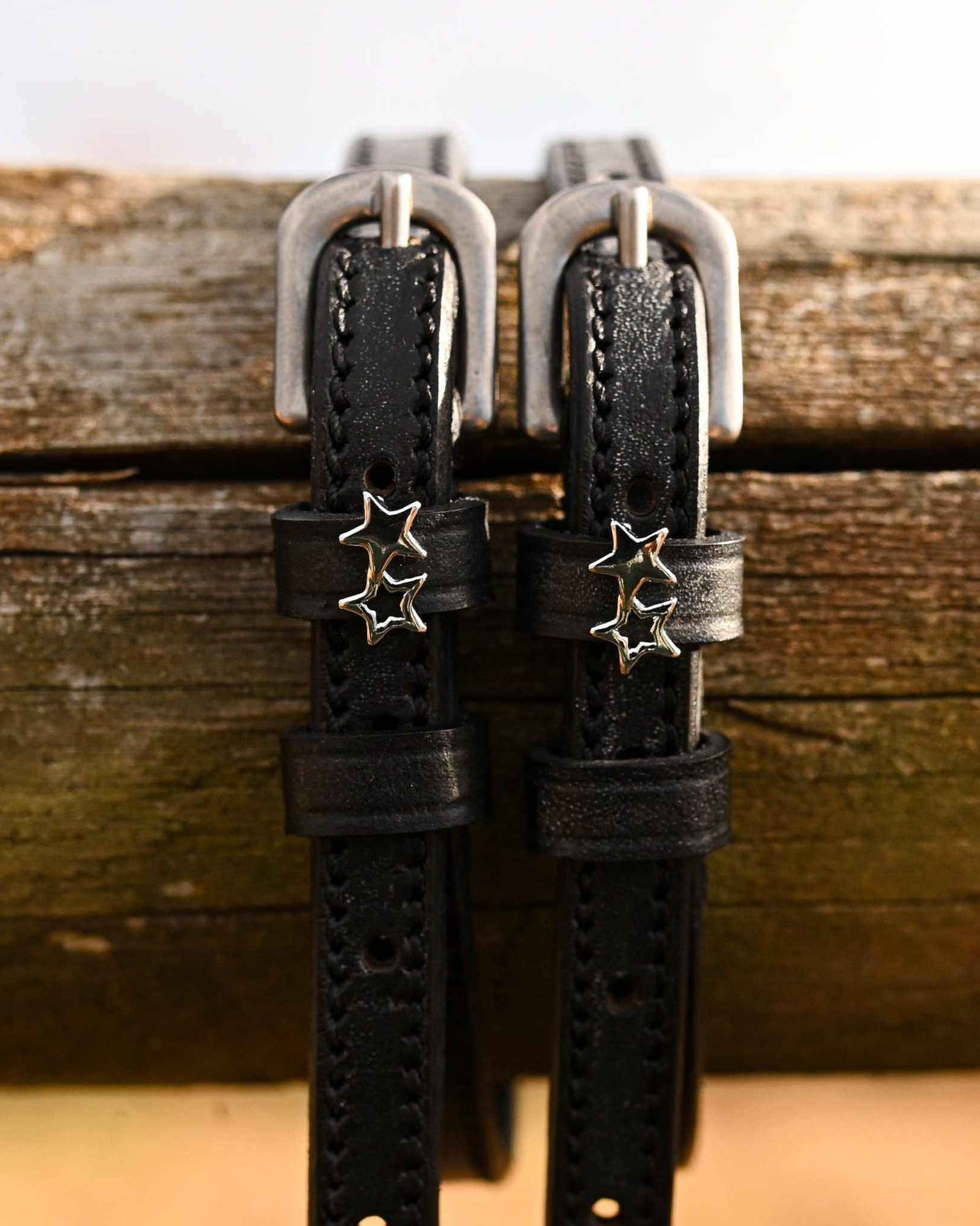 ManeJane double star spur straps hanging over a weathered wooden fence rail