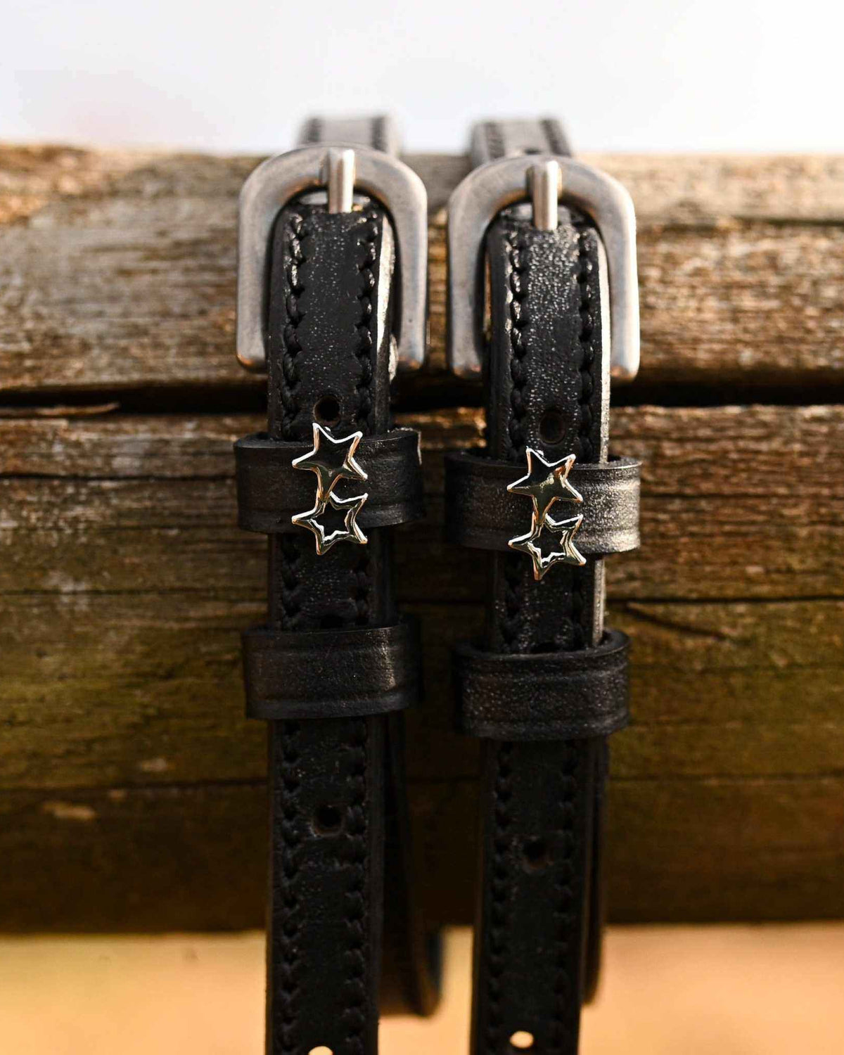 ManeJane double star spur straps hanging over a weathered wooden fence rail
