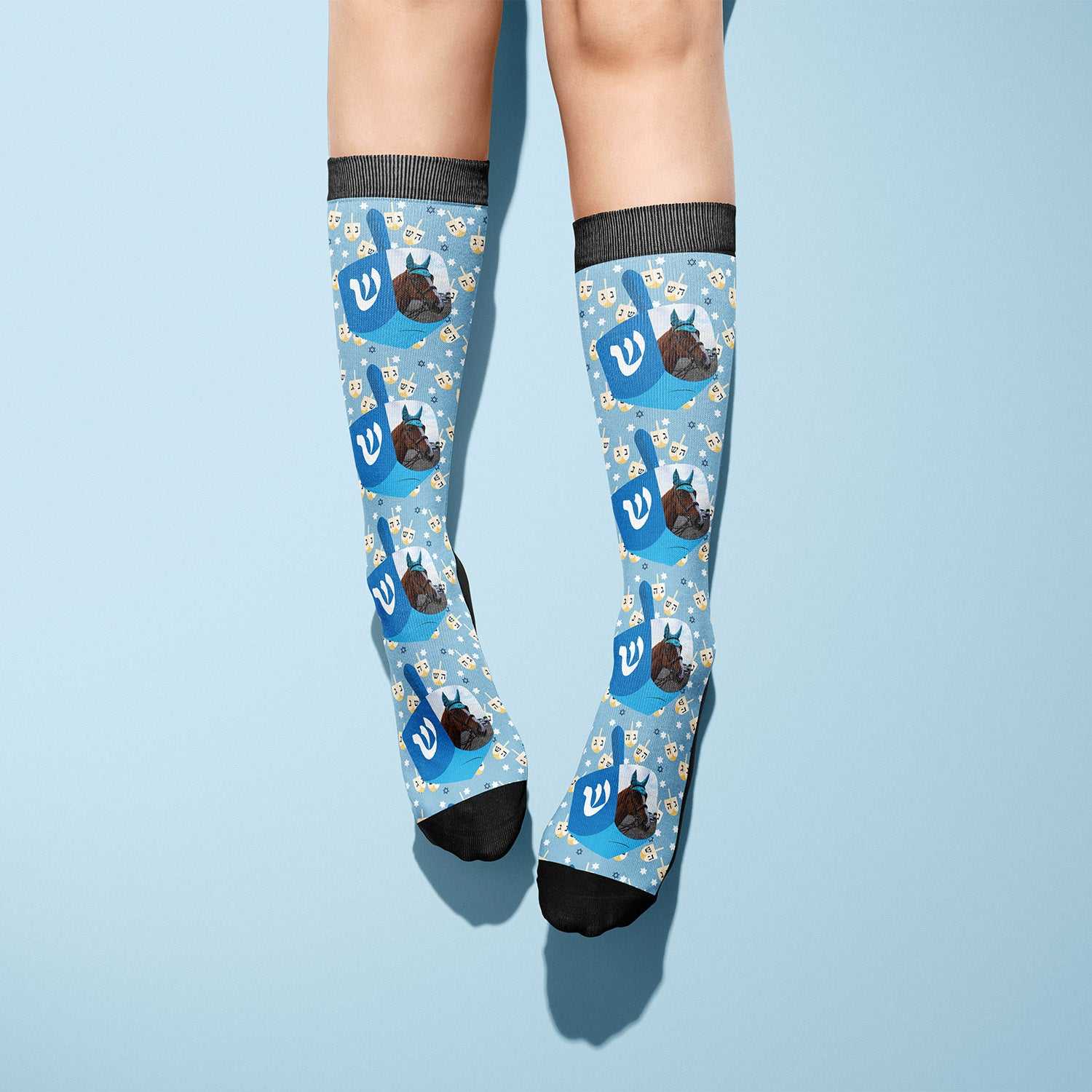 Custom socks featuring blue dreidel and Hanukkah-themed designs on light blue background worn on legs