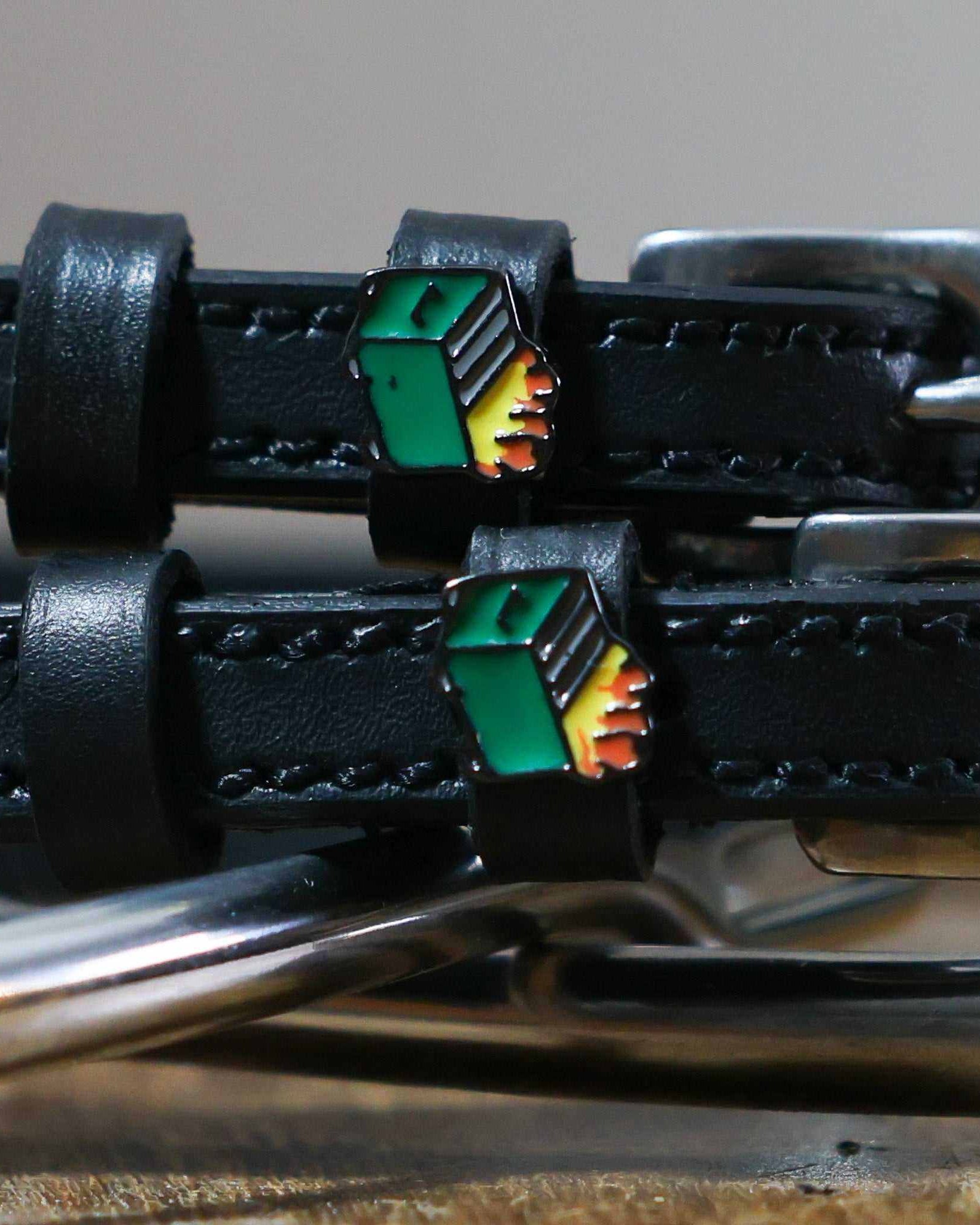Close-up of green dumpster fire enamel charms on black leather spur strap keepers