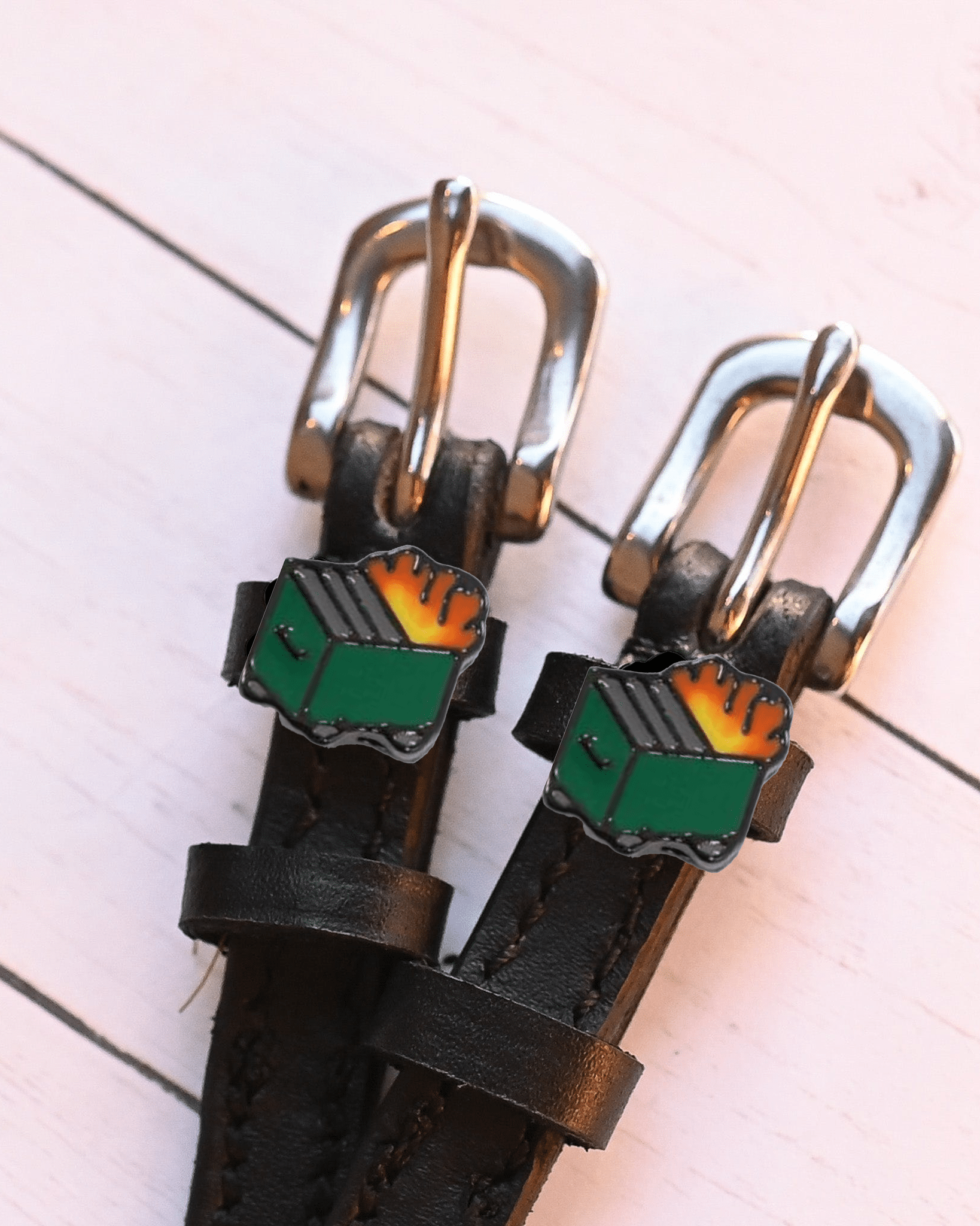 Close-up of dumpster fire charms on black leather spur straps on pink wood planks
