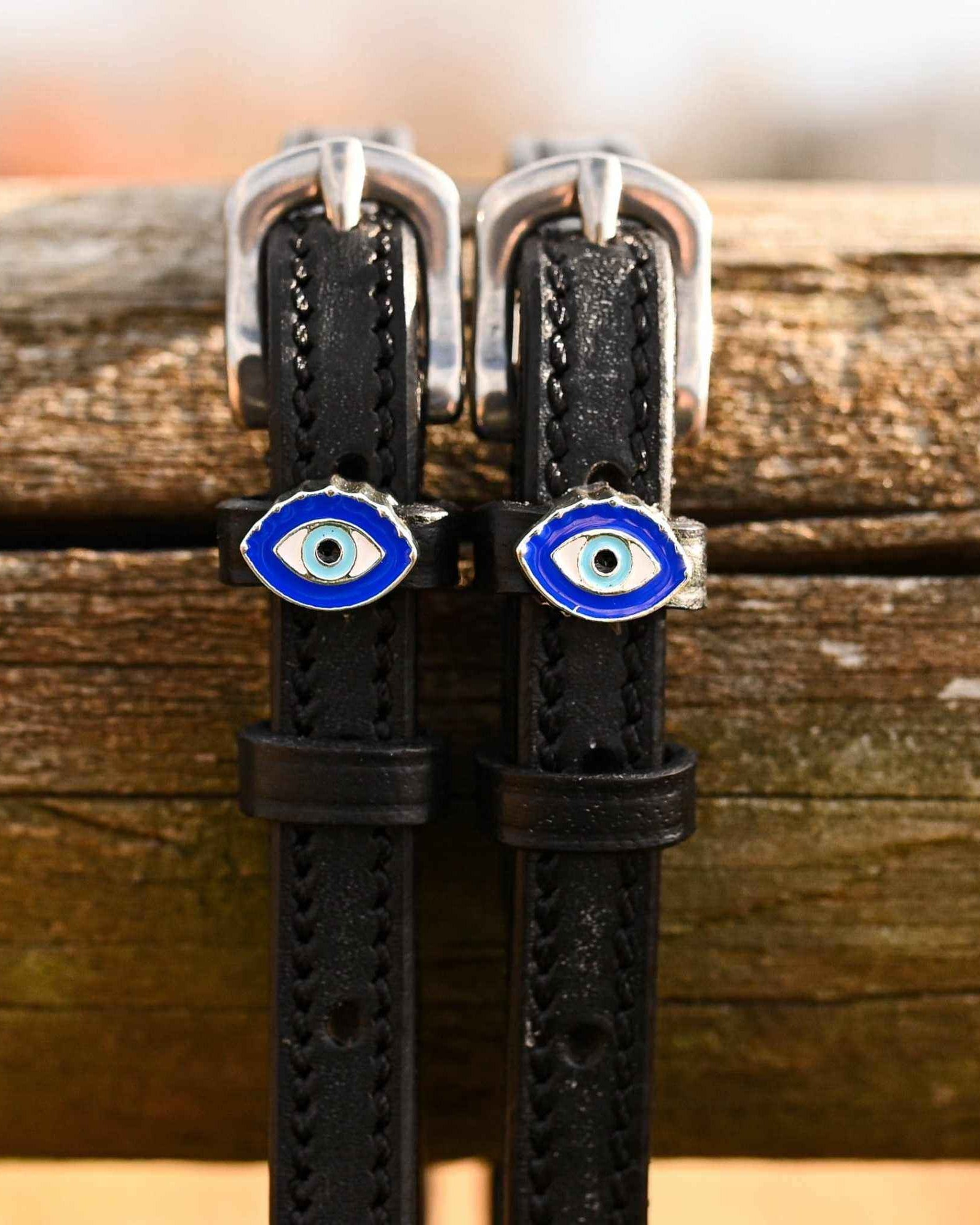 Close-up of blue evil eye charms on black leather spur straps over a wooden rail