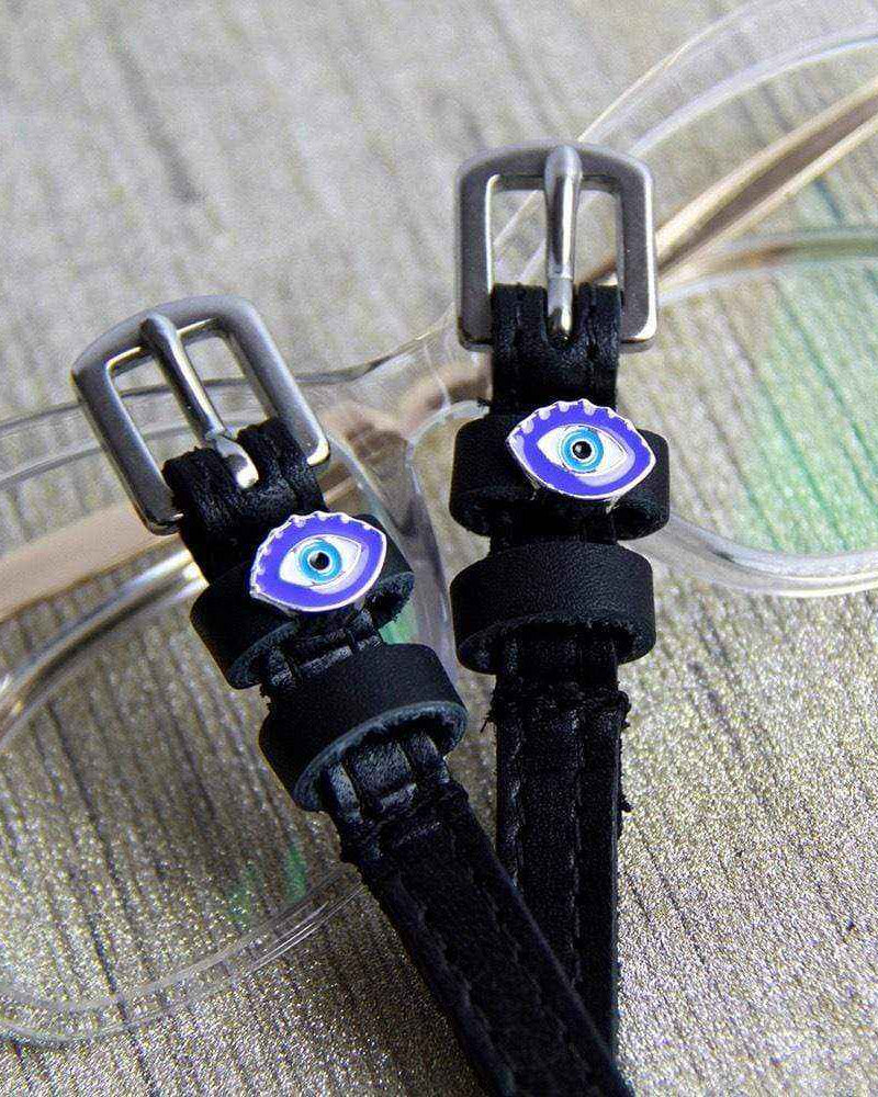 Blue evil eye spur straps resting on clear eyeglasses, ManeJane leather spur straps
