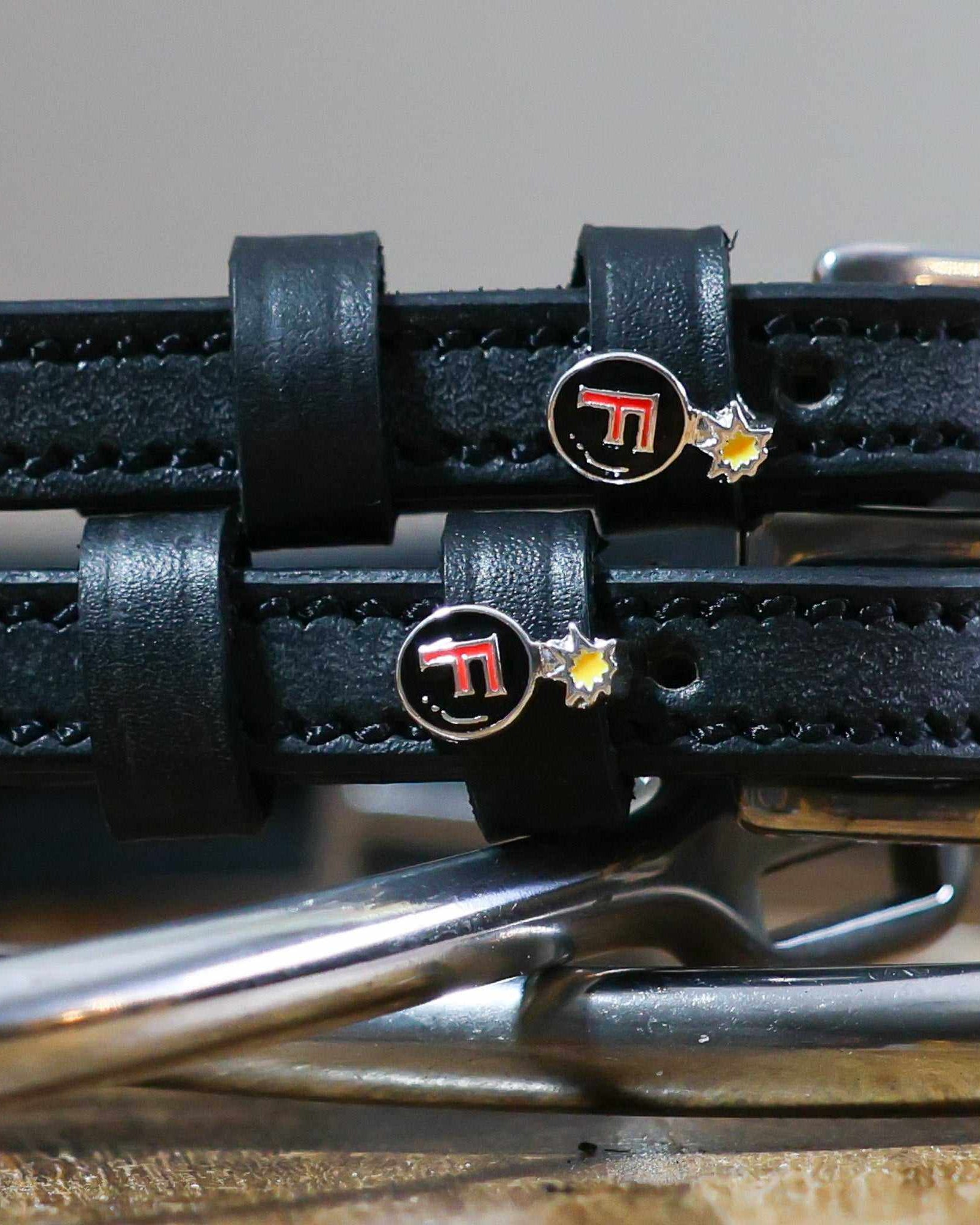 Close-up of red F-bomb charms on black leather ManeJane spur straps over spur hardware