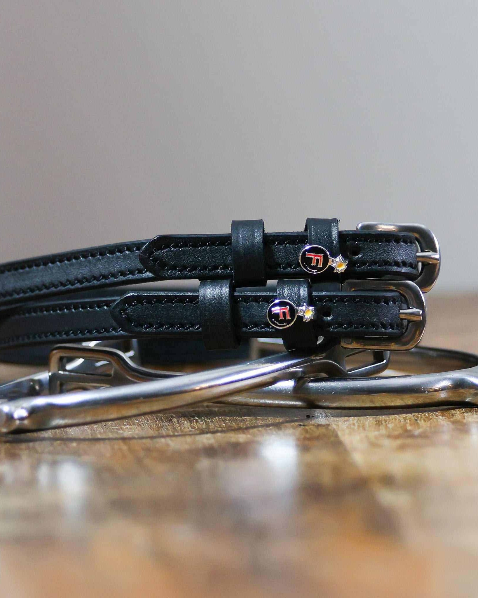F Bomb spur straps coiled beside silver spurs on a wooden table with red bomb charms