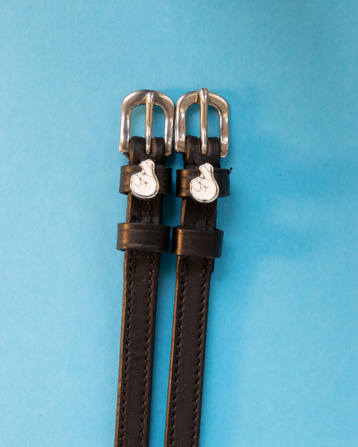 Black leather ManeJane spur straps with silver buckles and crossed-fingers charms on blue