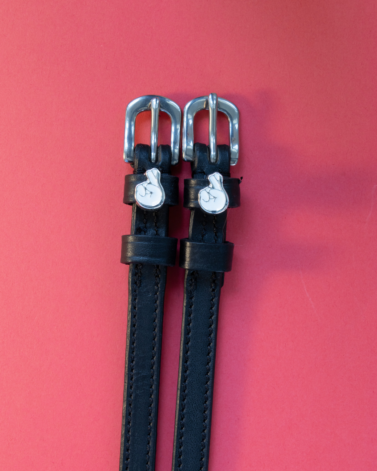 Pair of black leather crossed-fingers ManeJane spur straps on a red background