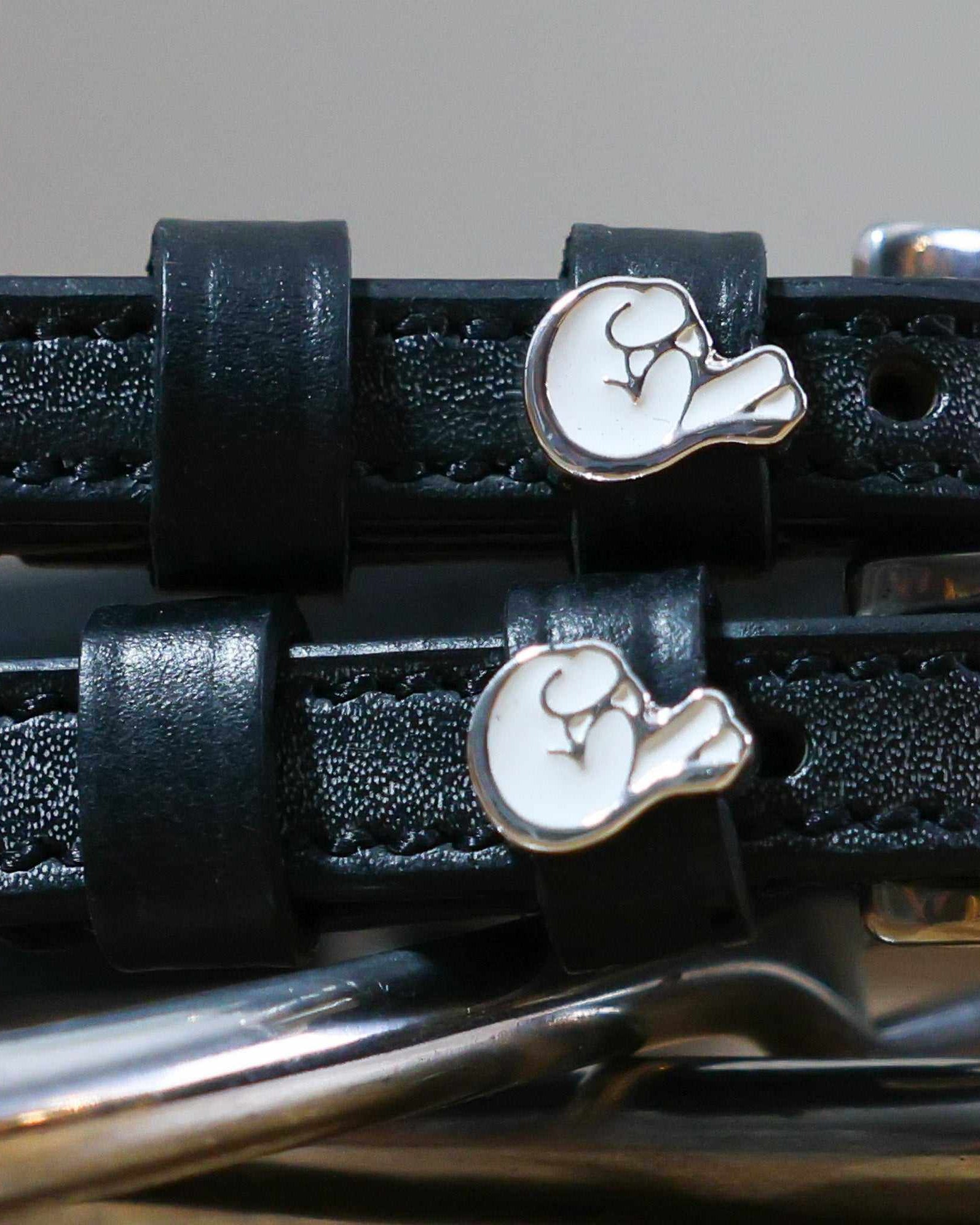 Close-up of white crossed-fingers charms on black leather ManeJane spur strap keepers