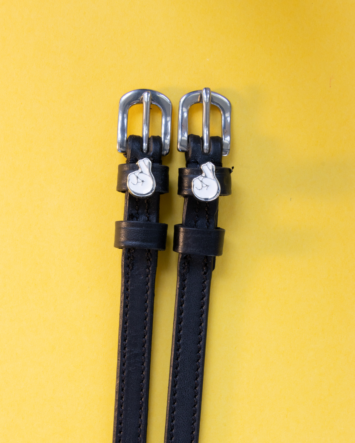 ManeJane crossed-fingers spur straps in black leather on a yellow background