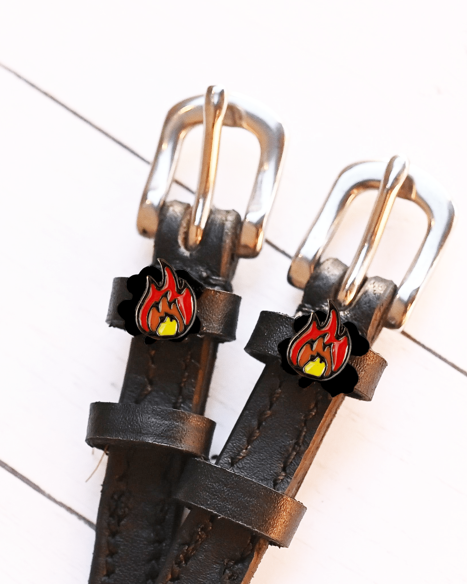 Close-up of red-and-orange flame charms on dark leather spur straps on white wood