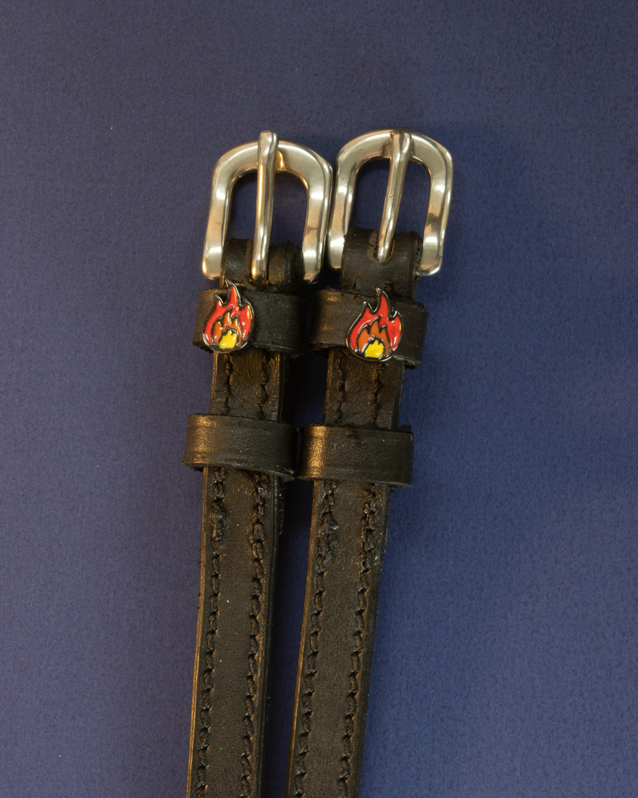 Pair of black leather flame spur straps with silver buckles on a navy background