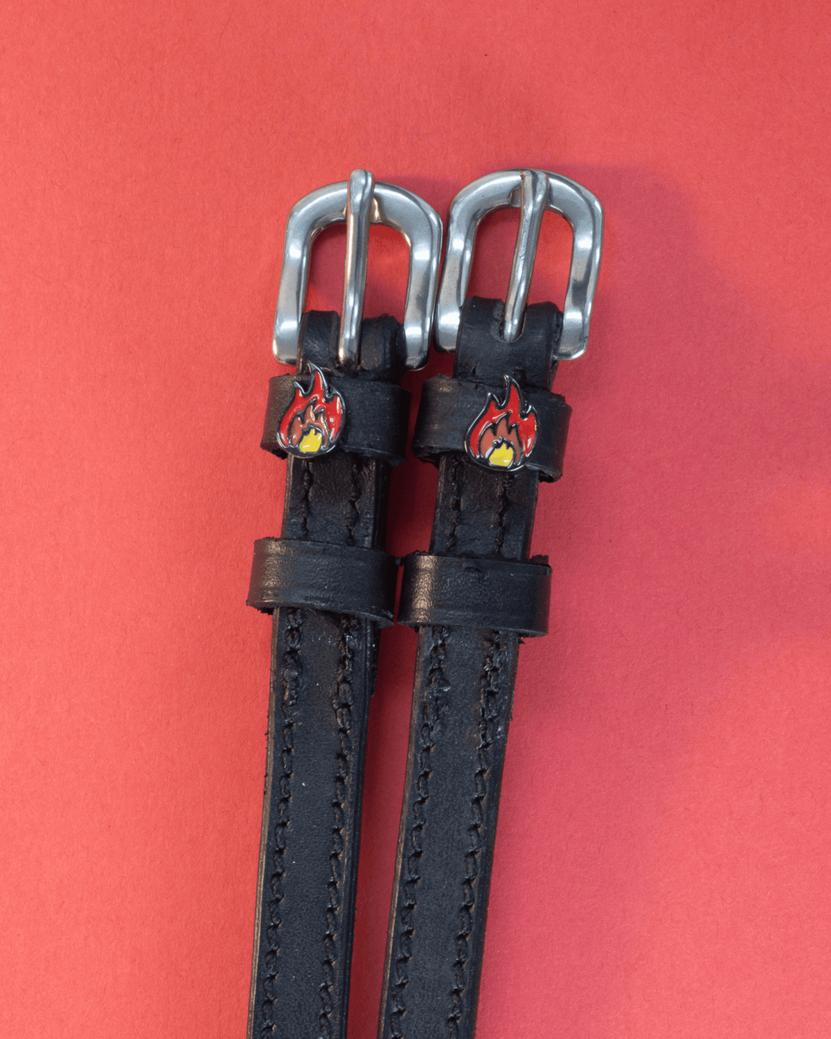 Black leather flame charm spur straps with silver buckles on a red background