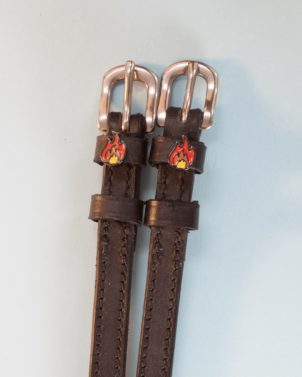 Brown leather flame spur straps with rose-gold buckles and fire charms, flat-lay
