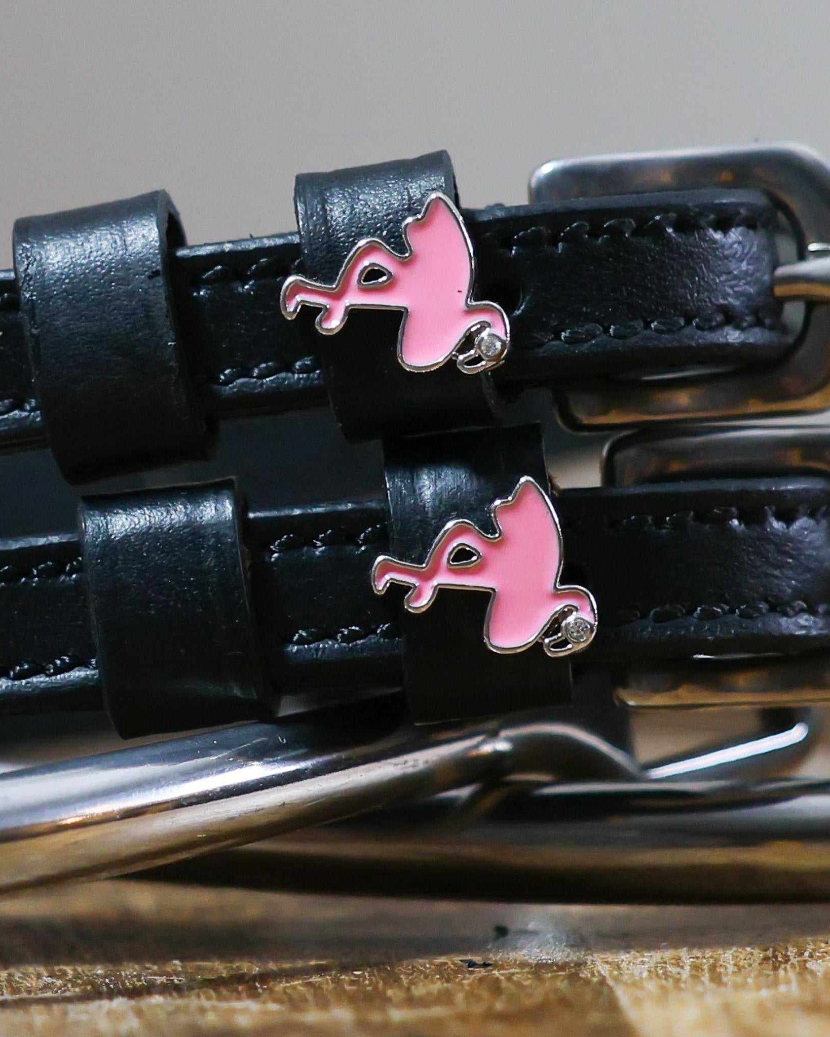 Close-up of pink enamel flamingo charms on black leather spur strap keepers