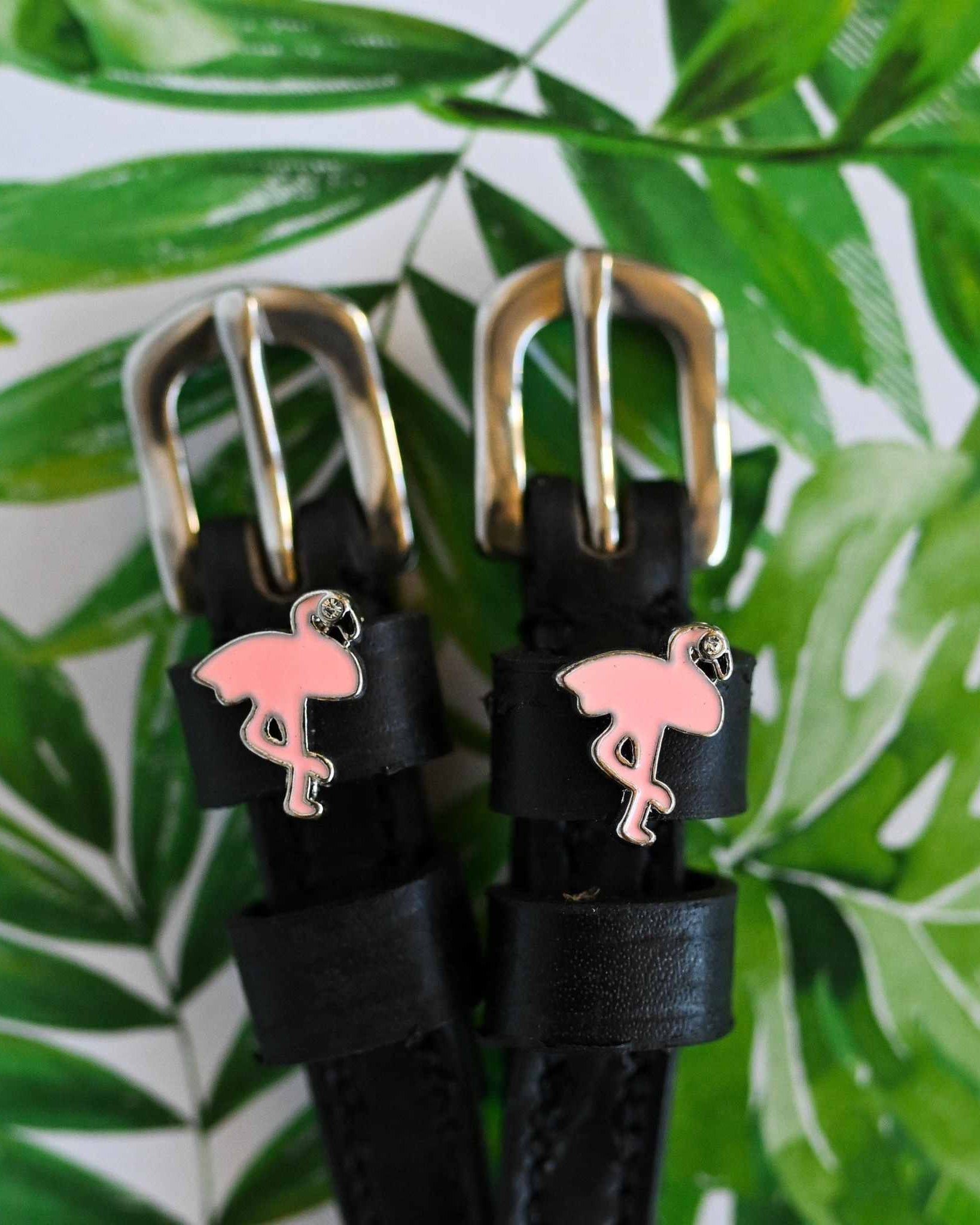 Flamingo charm spur straps against a tropical palm-leaf print background