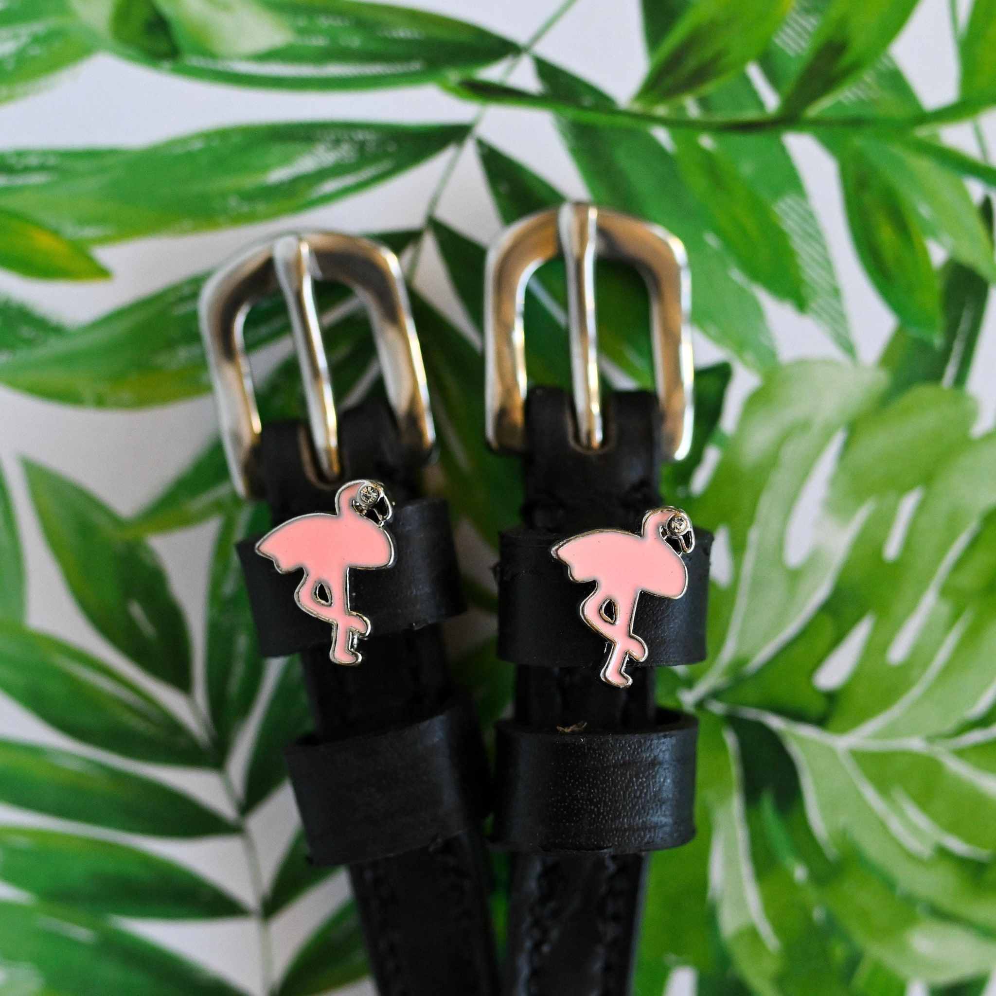 Flamingo charm spur straps against a tropical palm-leaf print background