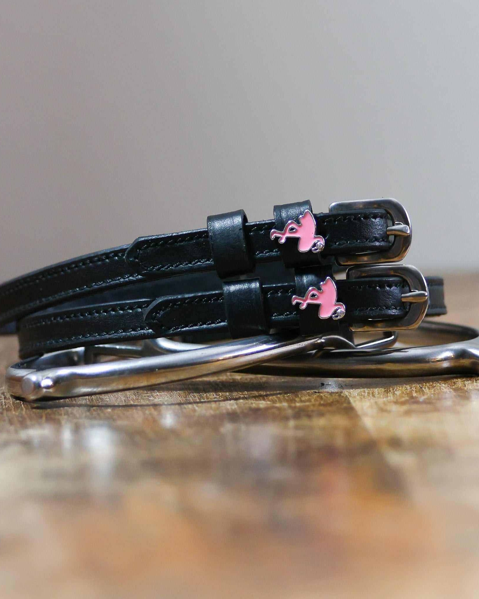Black leather flamingo spur straps coiled beside a stirrup on wood