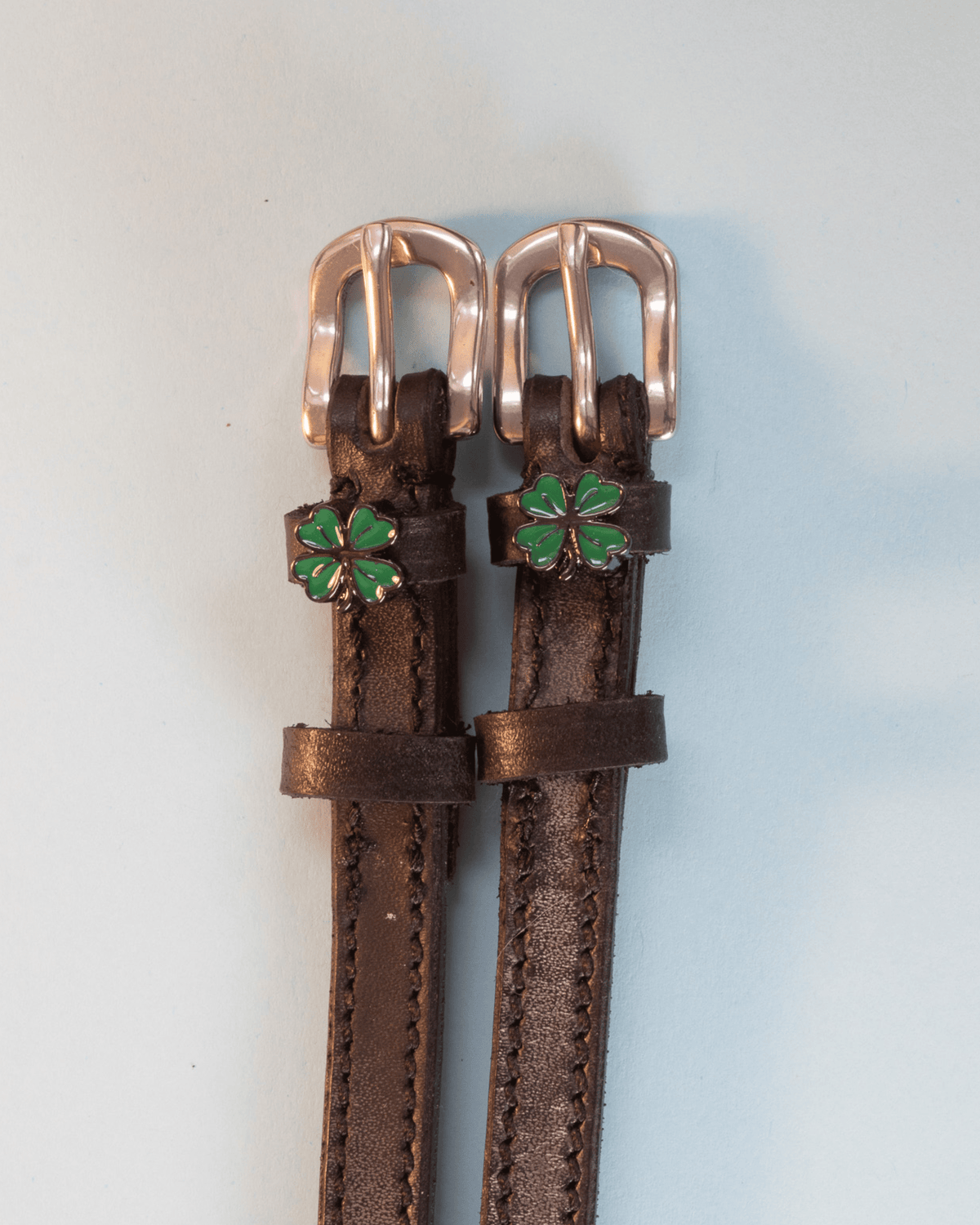 Brown leather ManeJane clover spur straps with rose-gold buckles and green clover charms