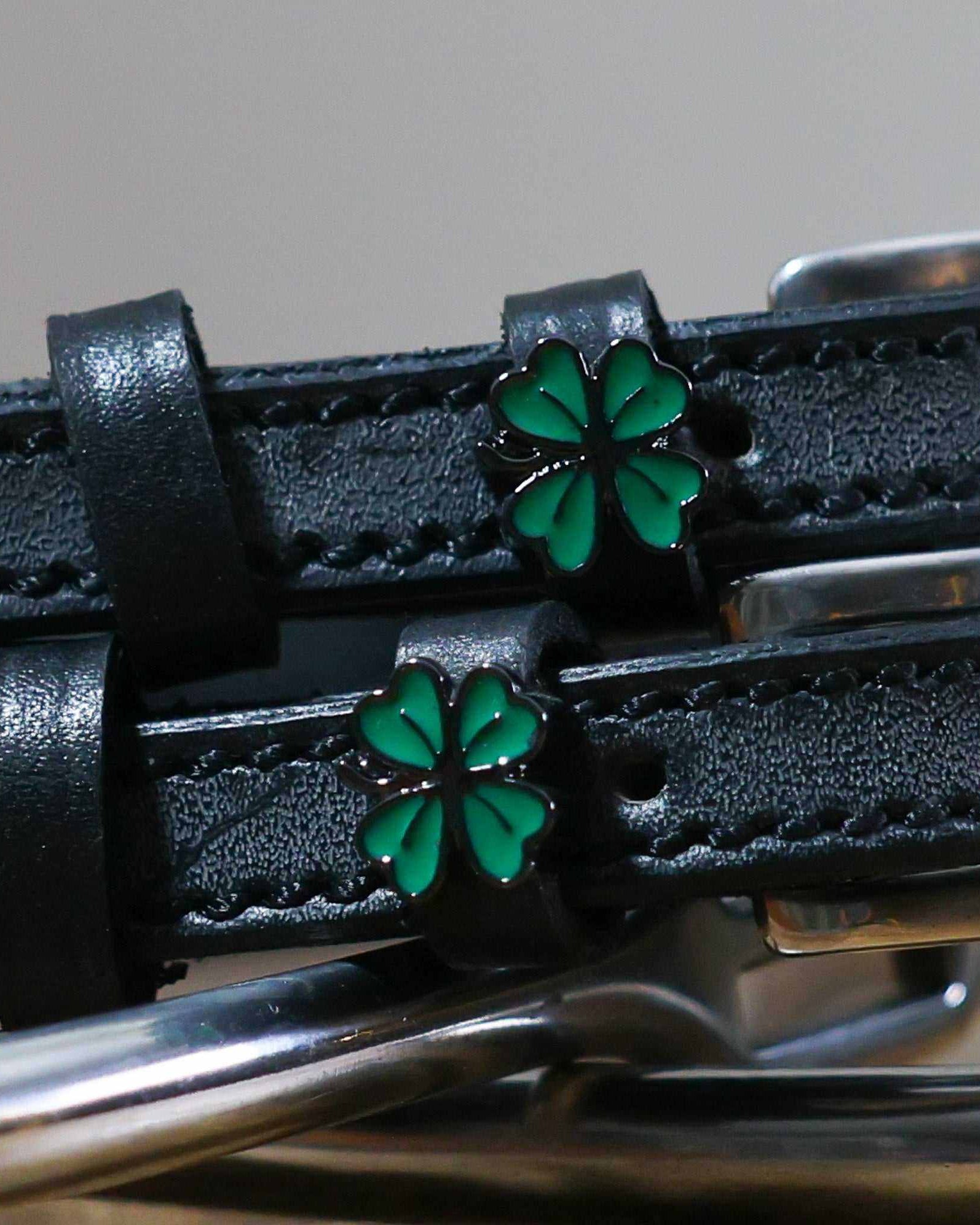 Close-up of green enamel four leaf clover charms on black leather ManeJane spur straps
