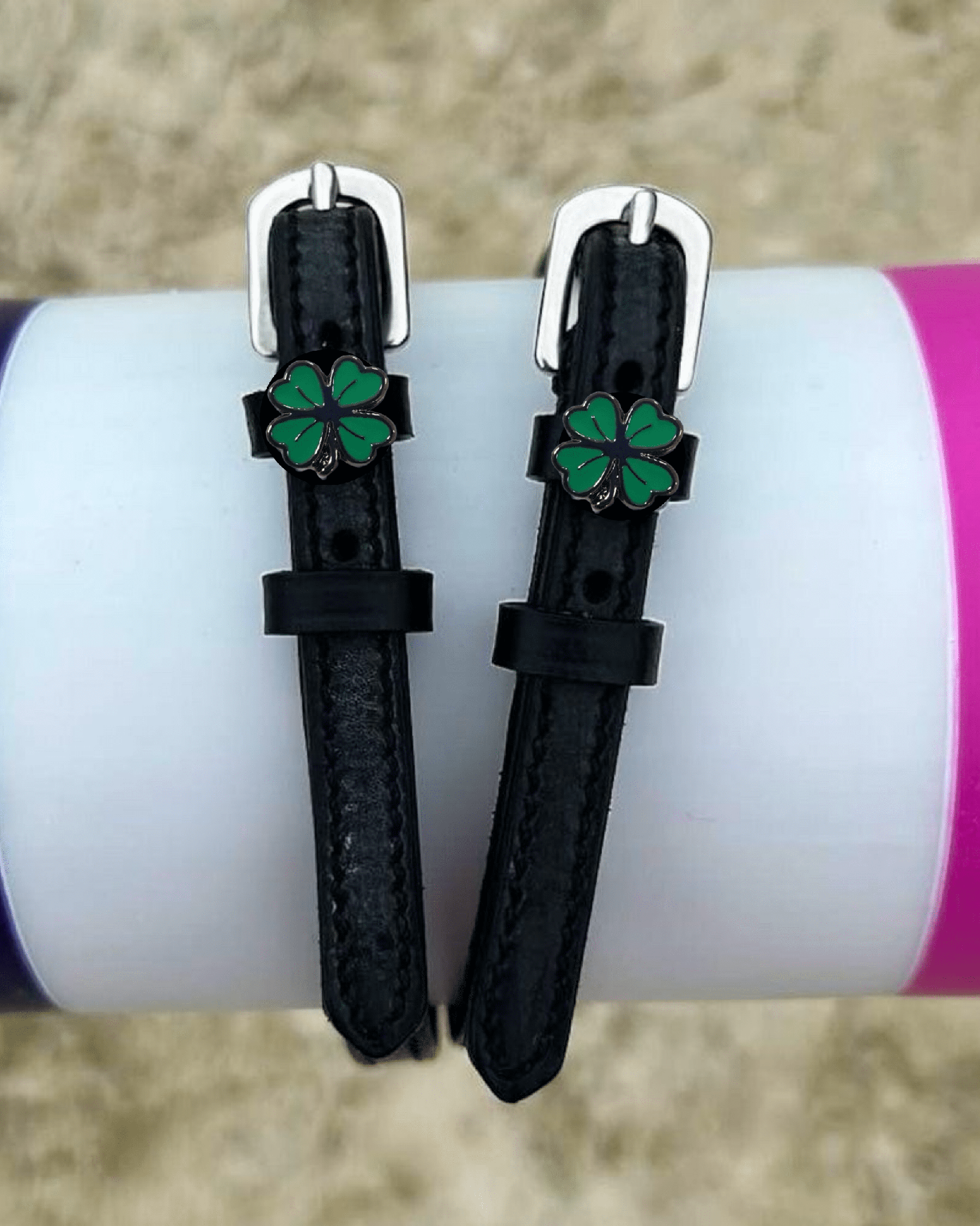 Four leaf clover spur straps draped over a purple and pink jump rail, green clover charms