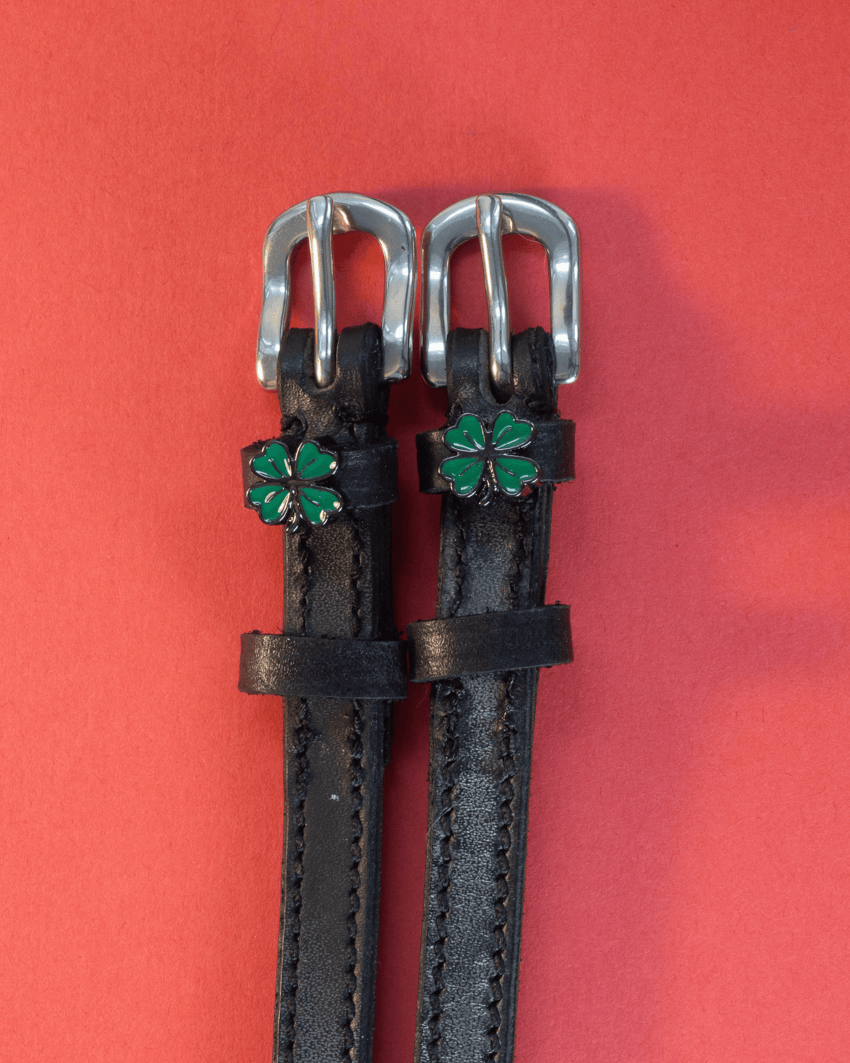 ManeJane clover spur straps with silver buckles flat on a red background, green clover charms